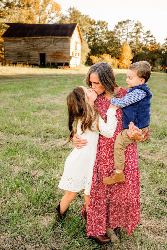 Daughter gives her mom a hug and kiss while mommy holds their youngest son on her hip