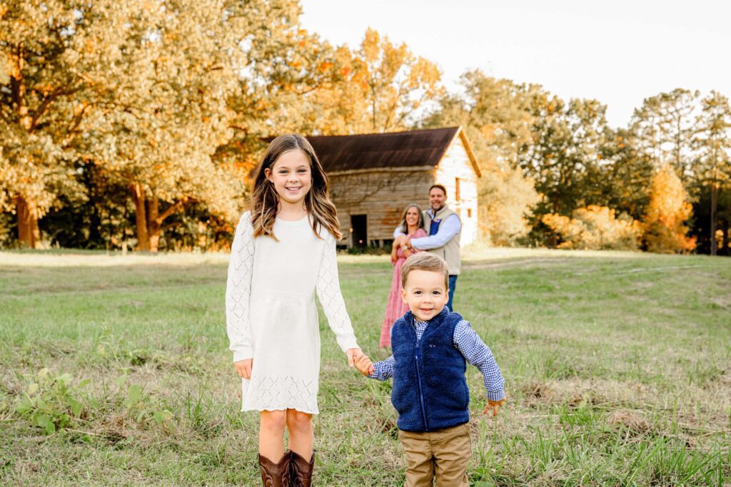 Children standing hand in hand laughing with parents standing behind them with a barn in the background