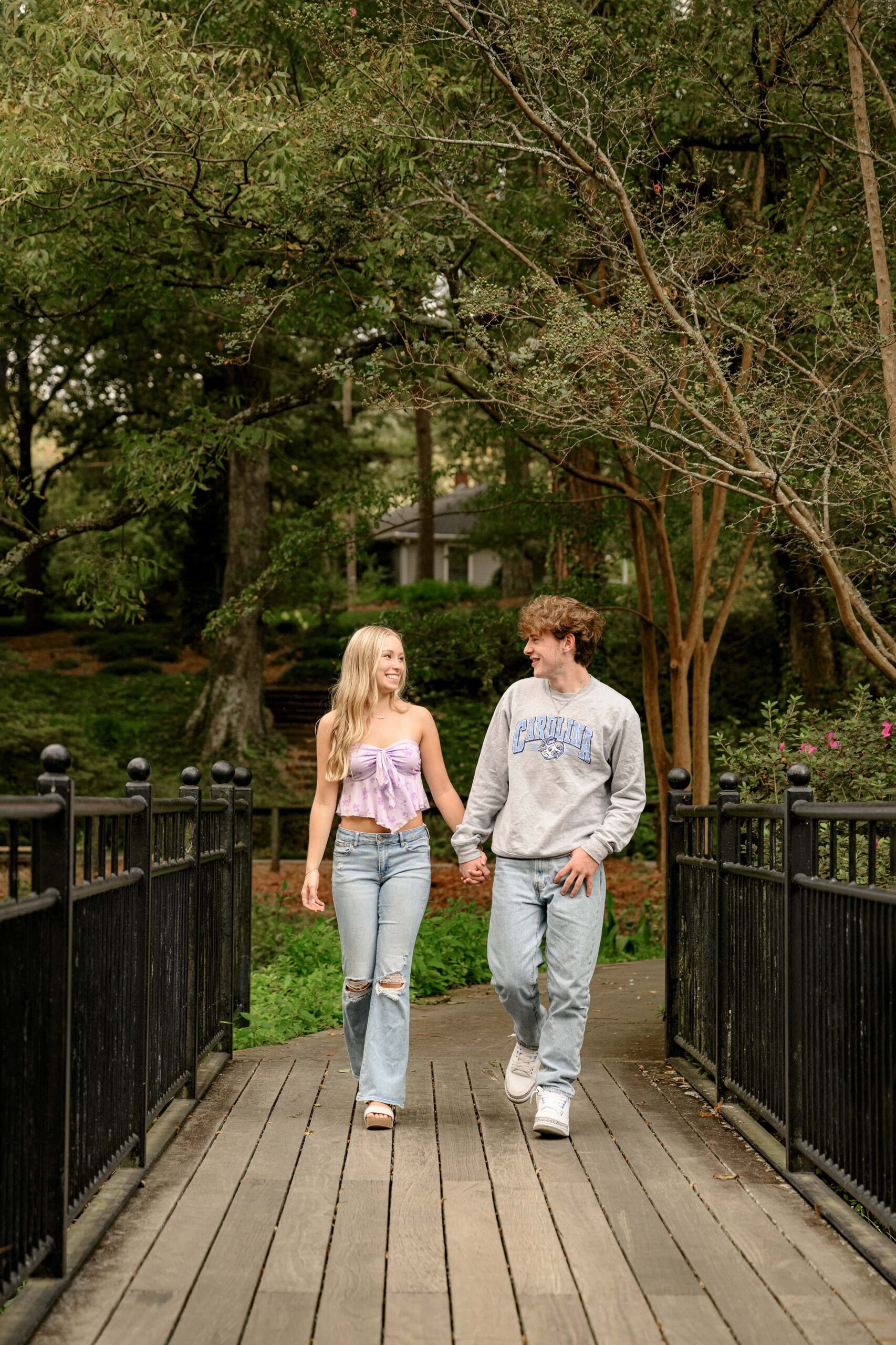 senior girl holds hands with her boyfriend and walks across rock hill sc garden bridge