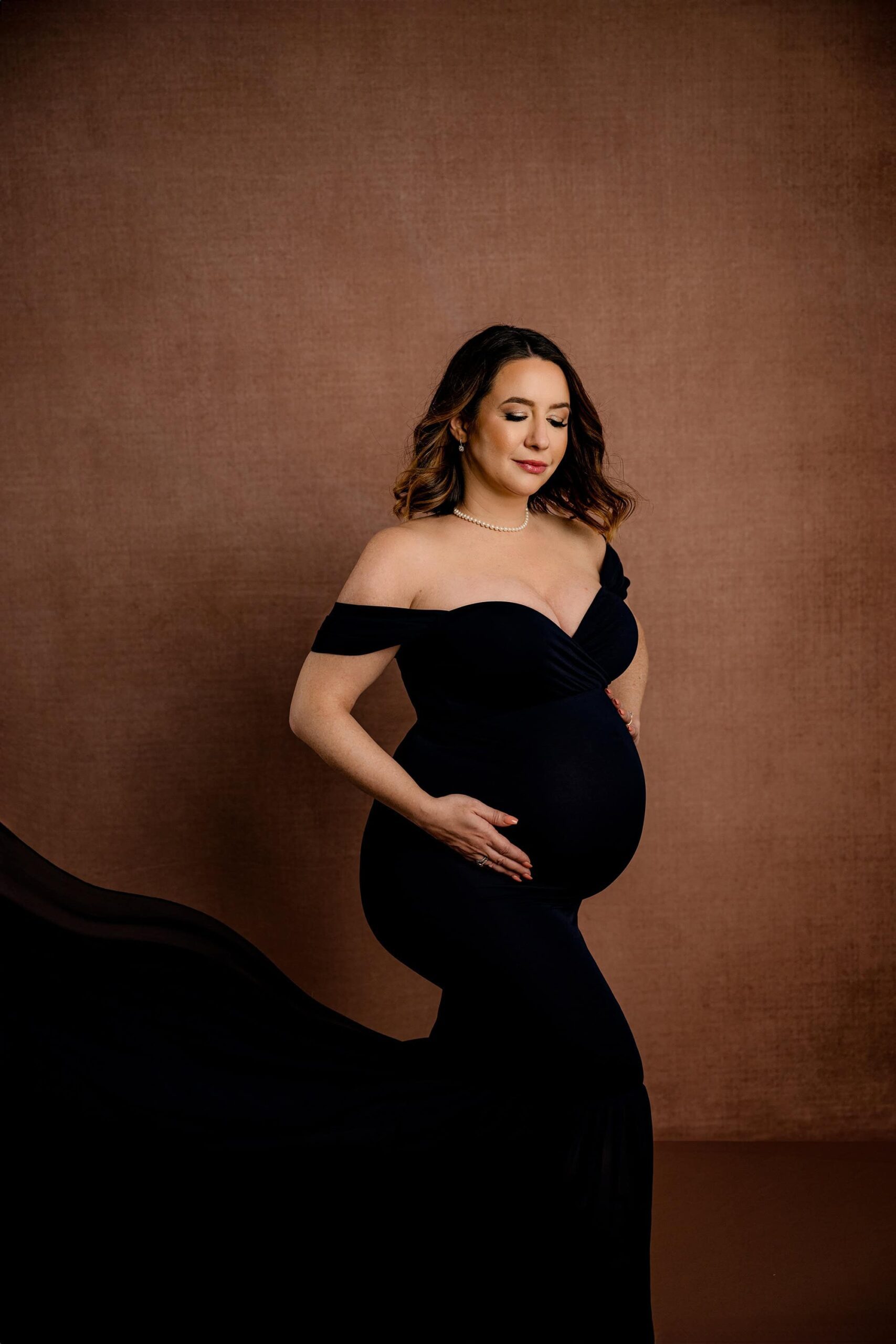 expectant mother poses with her hands on her belly during her. Waxhaw, NC studio maternity session