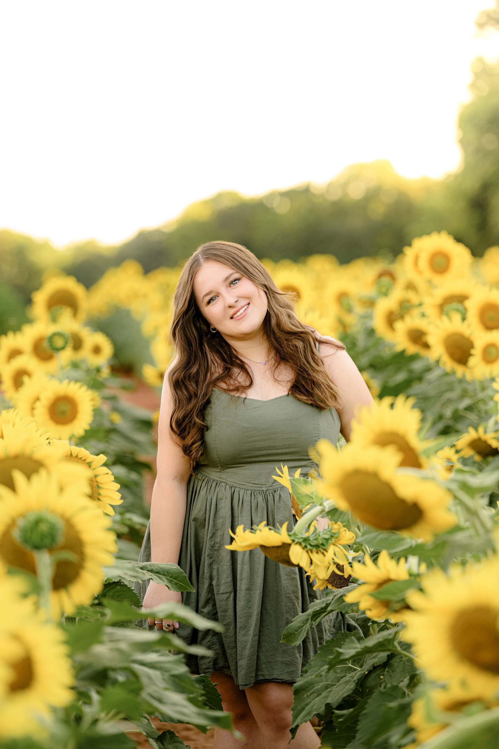 dark hair senior in a green dress standing in a field
