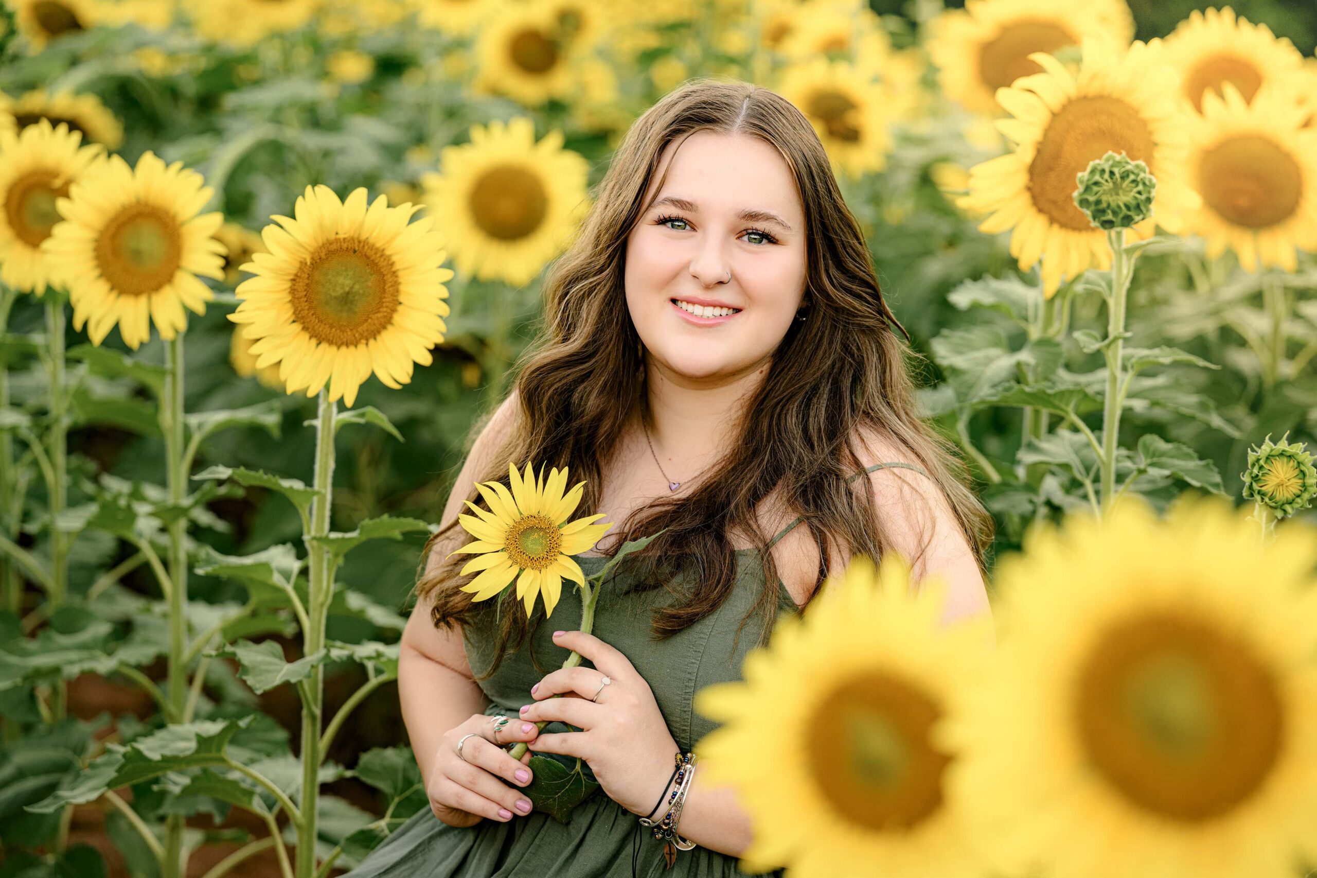 Cuthbertson High School graduate sitting among vibrant sunflowers, smiling during her flower senior session.