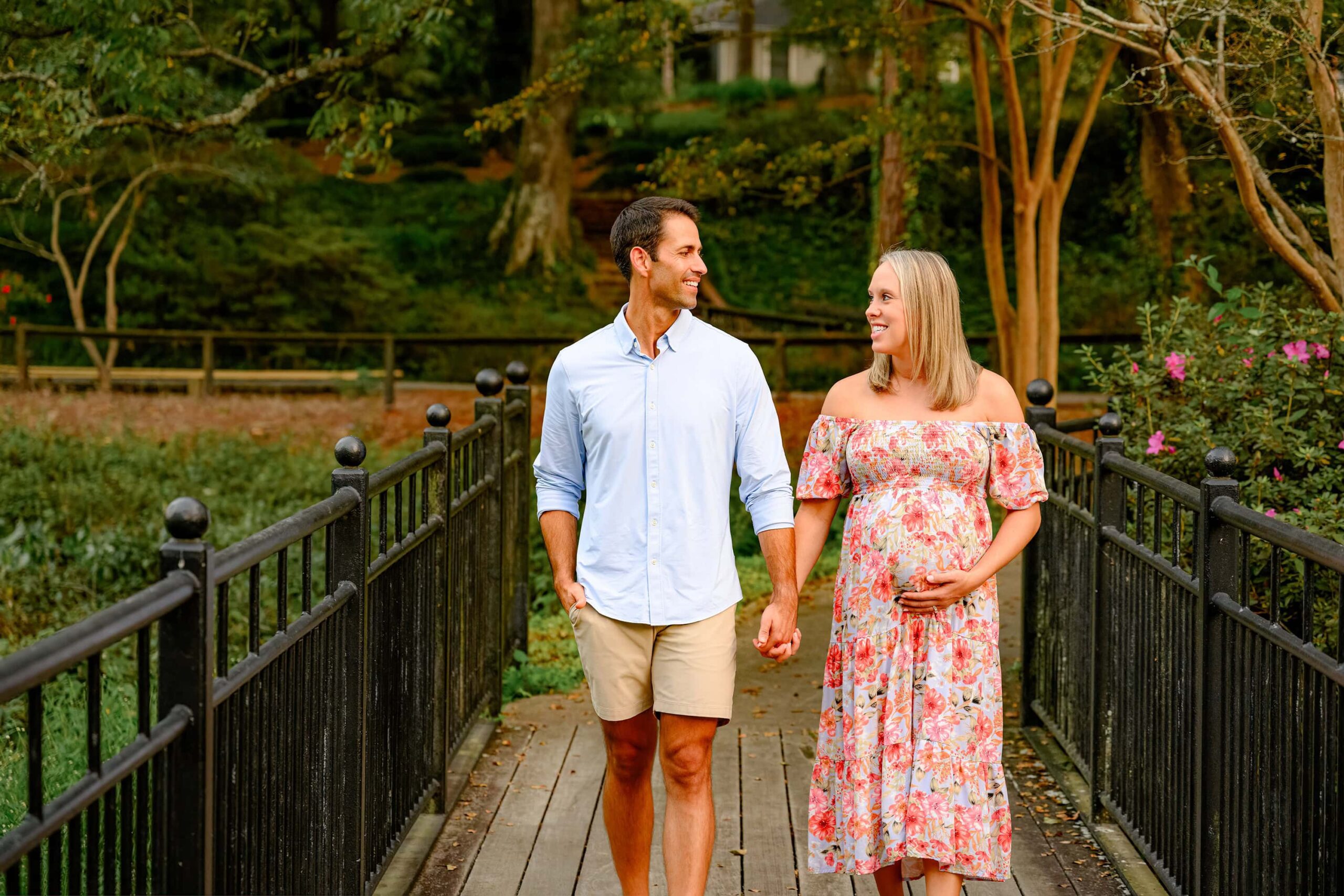 Charlotte couple posed on a bridge holding hands looking into each others eyes enjoying the excitement of their outdoor maternity photography session.