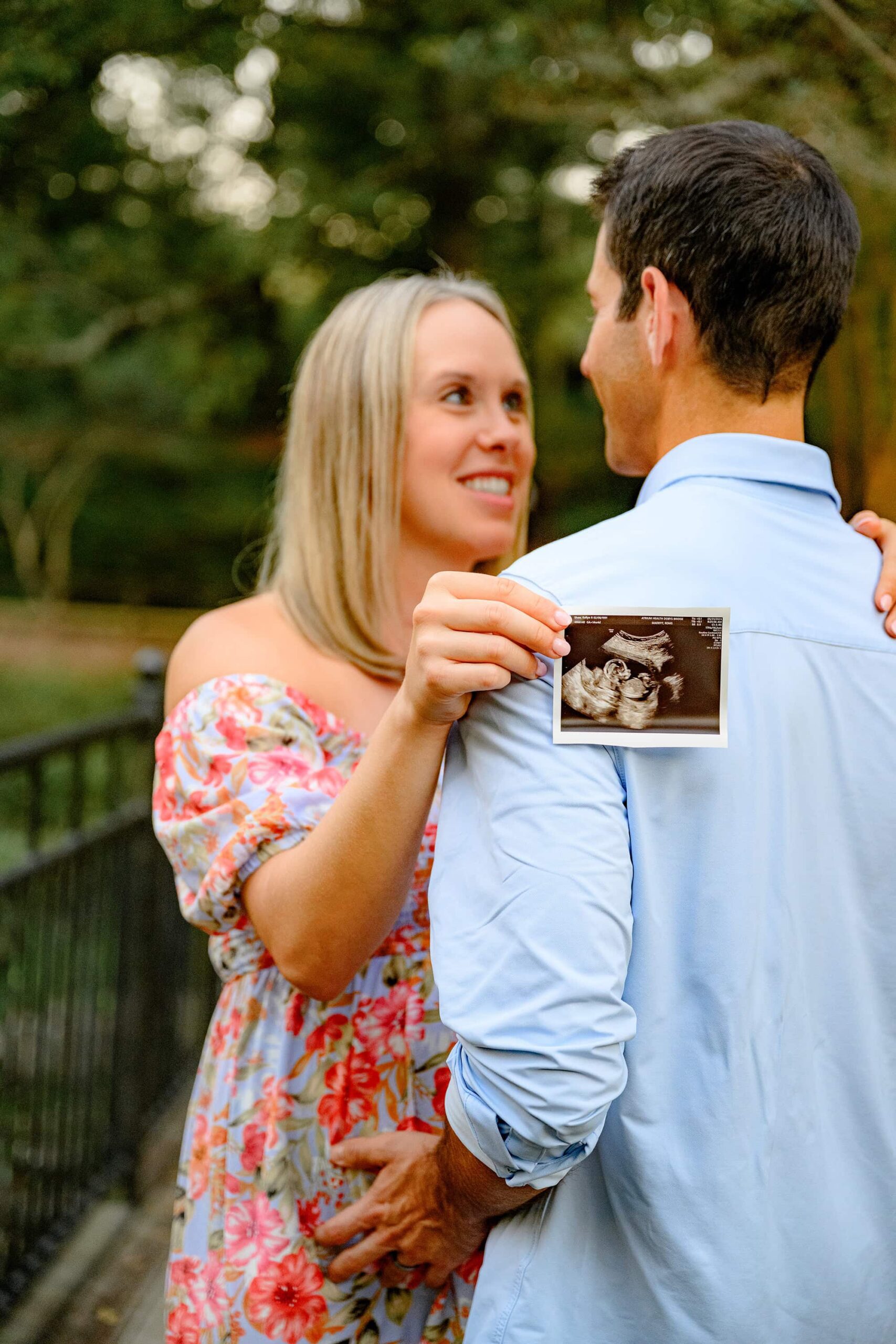 expectant couple from the charlotte nc area looks at each other while mom holds an ultrasound in a Rock Hill, SC flower garden