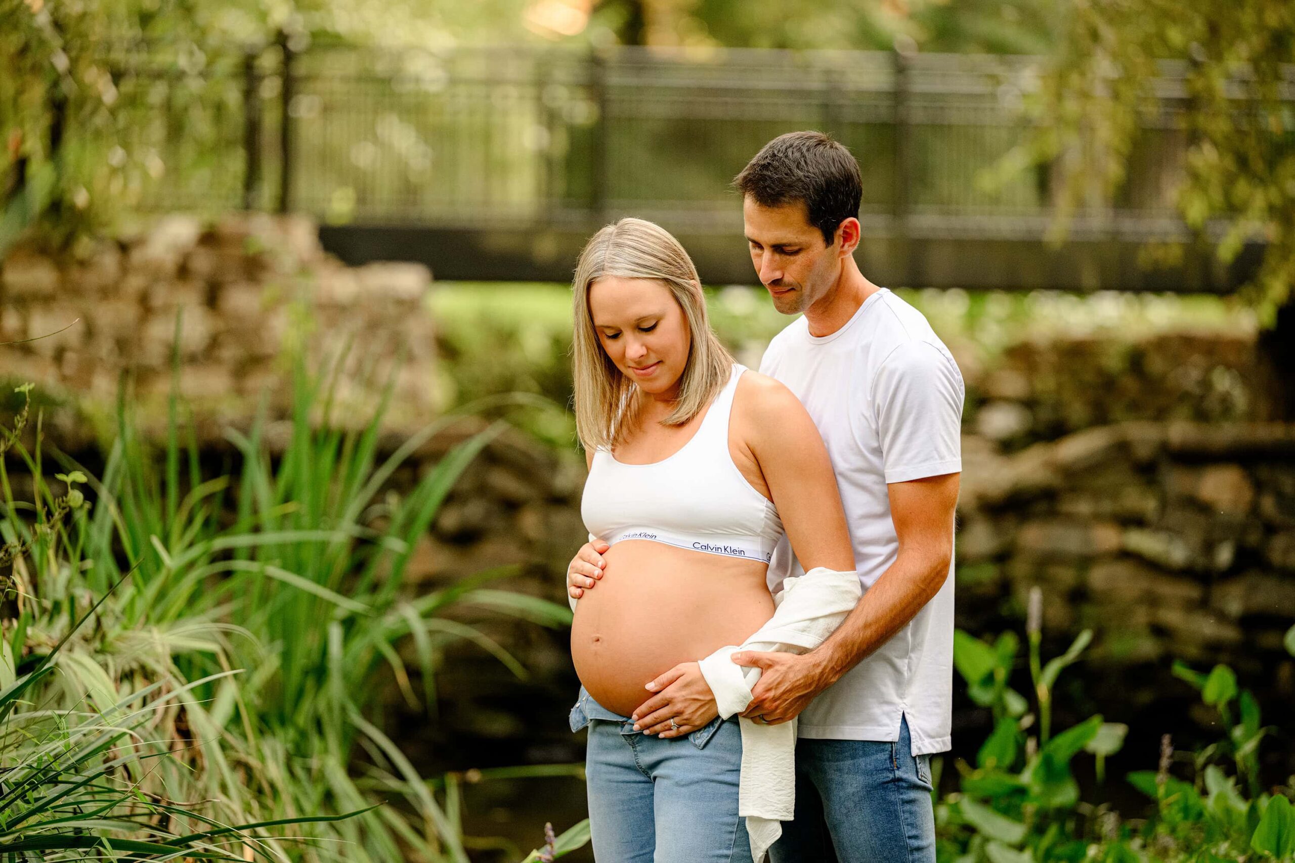 expecting Charlotte parents mother and father posed looking at her baby bump while wearing casual sports bra and jeans