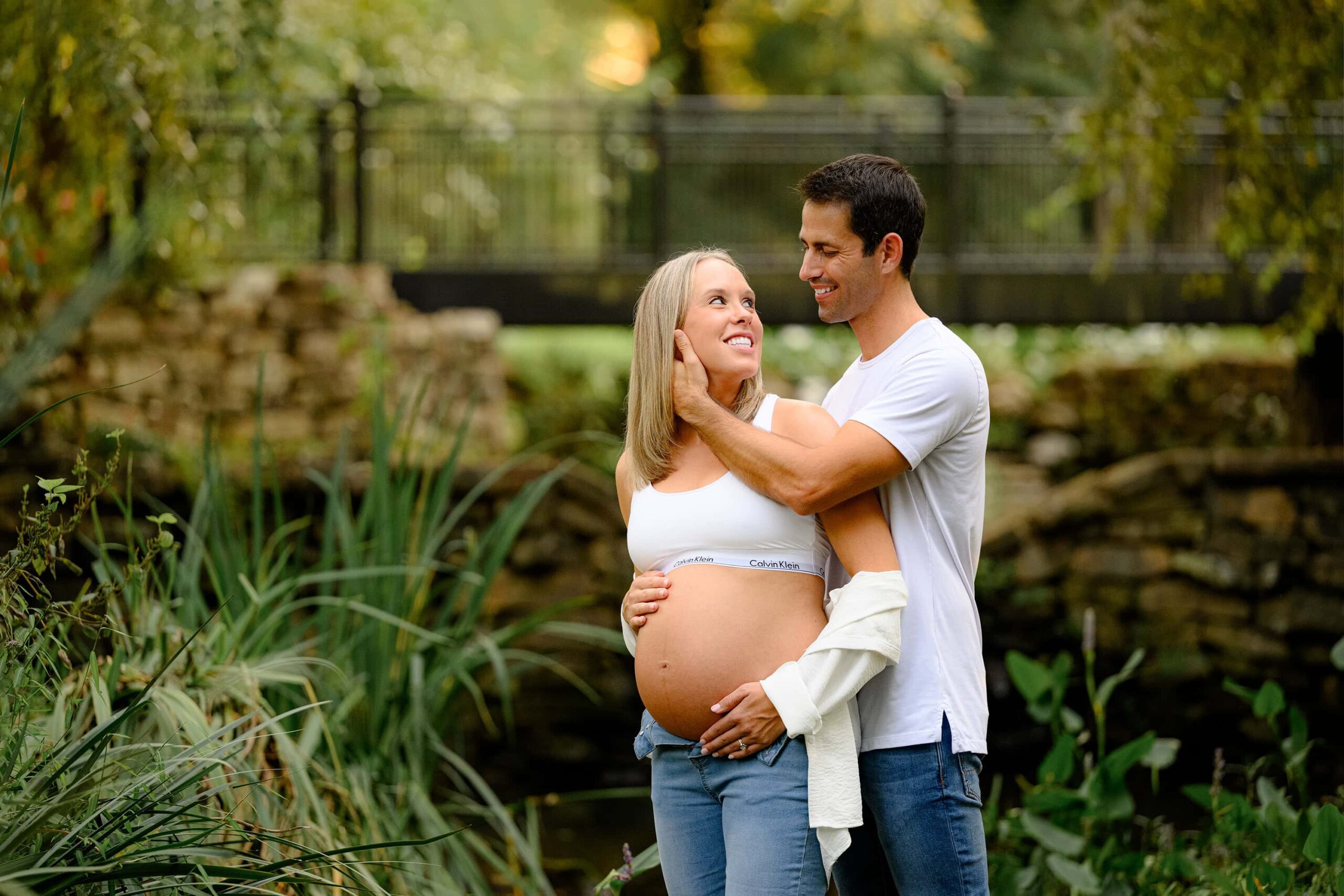 Charlotte expecting couple casually dressed in jeans and white shirts standing together in a south carolina garden
