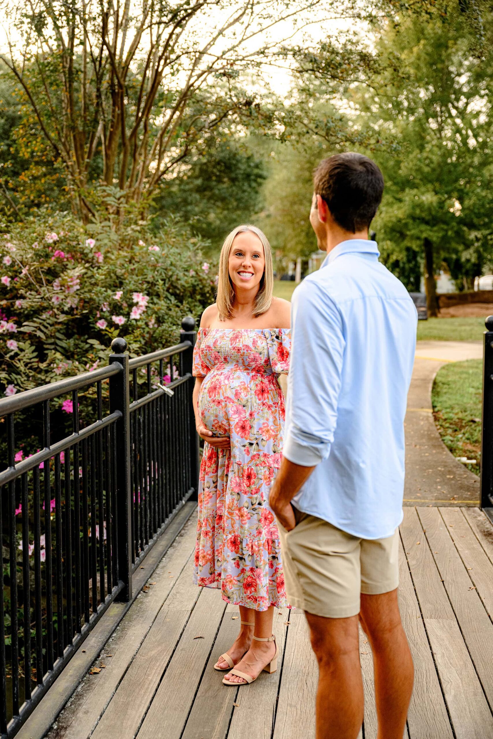 Charlotte area expectant mother dressed in floral dress exchanges a sweet smile with her husband during their maternity session in a rock hill flower garden