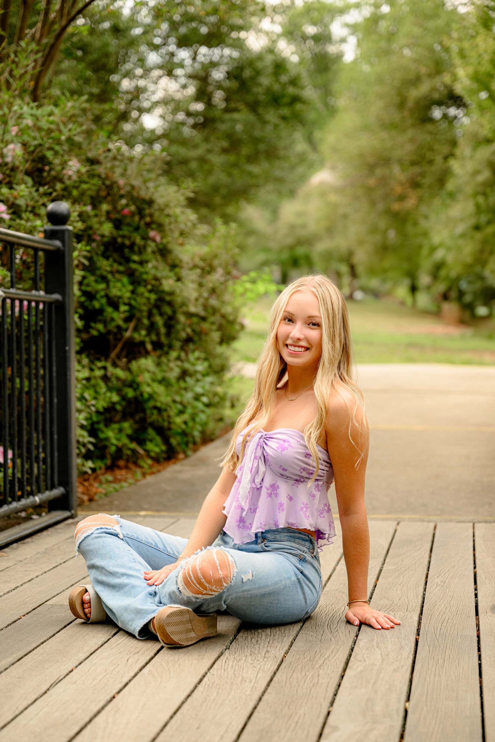 Class of 2025 senior from Cuthbertson High School dressed in jeans and purple crop top sitting cross legged on a bridge in rock hill, sc