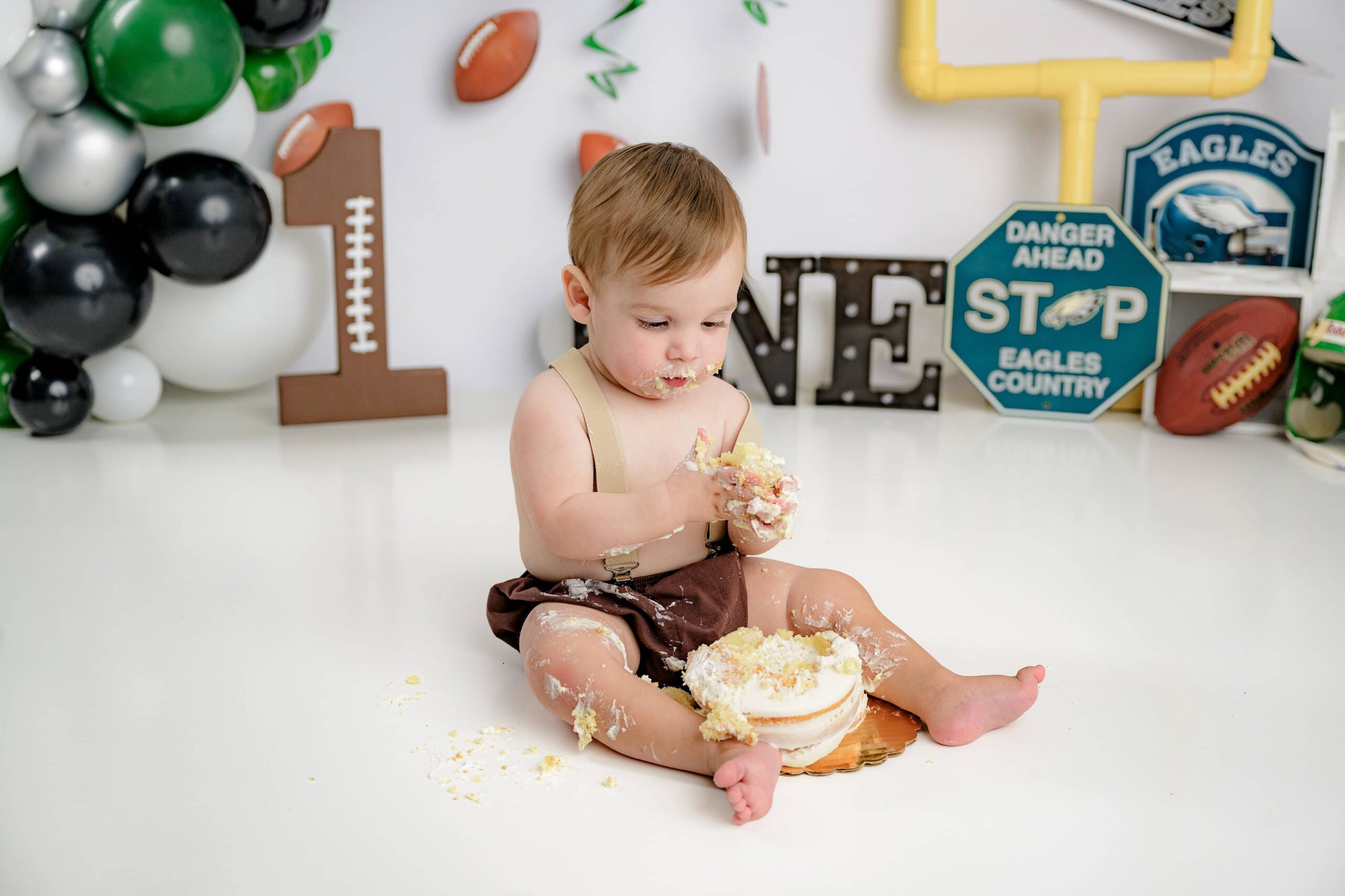Little boy playing in his smash cake wearing suspenders