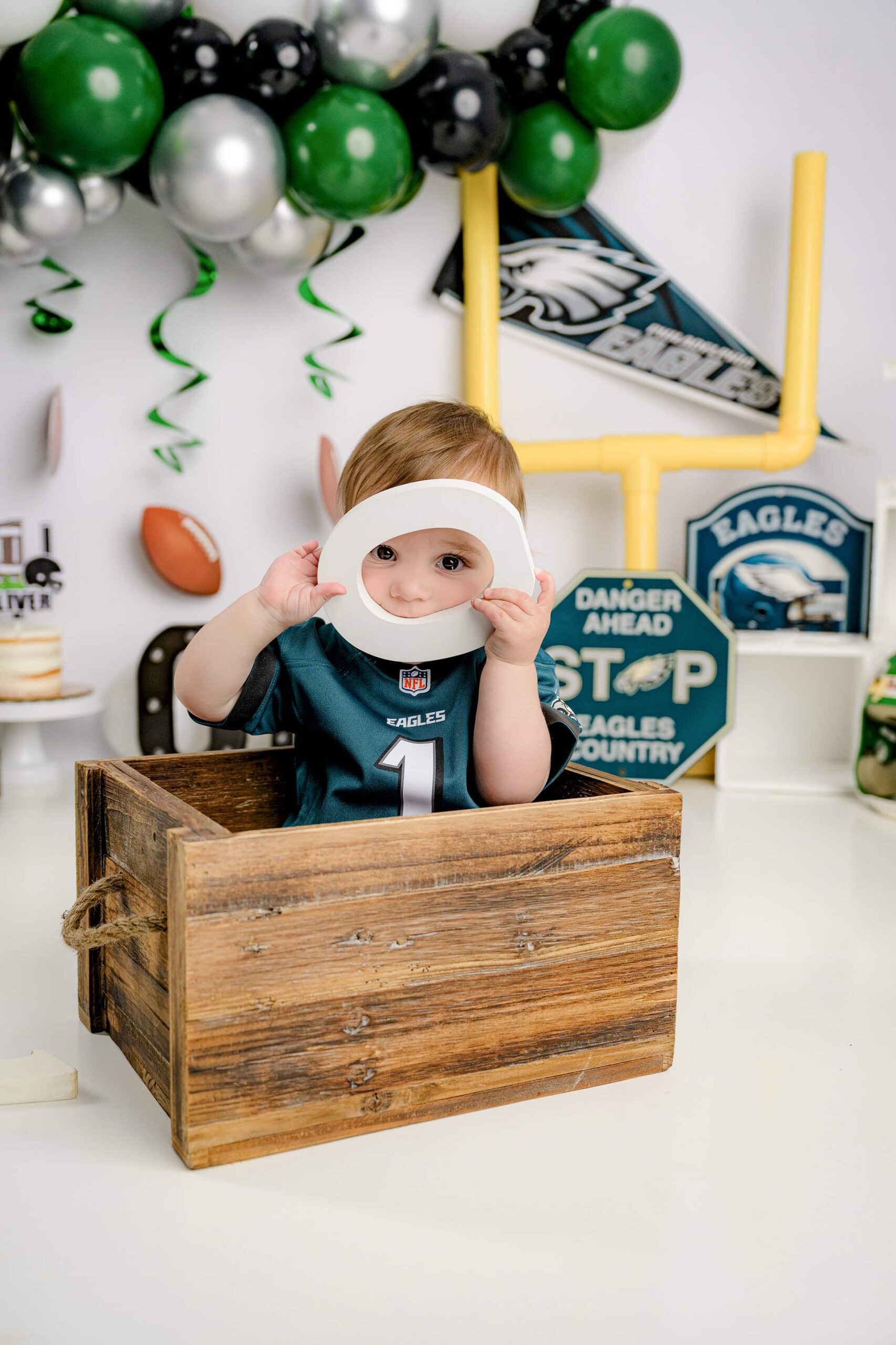 First birthday Eagles football cake smash session featuring a joyful baby, a custom football-themed cake, and festive decorations in green and white.