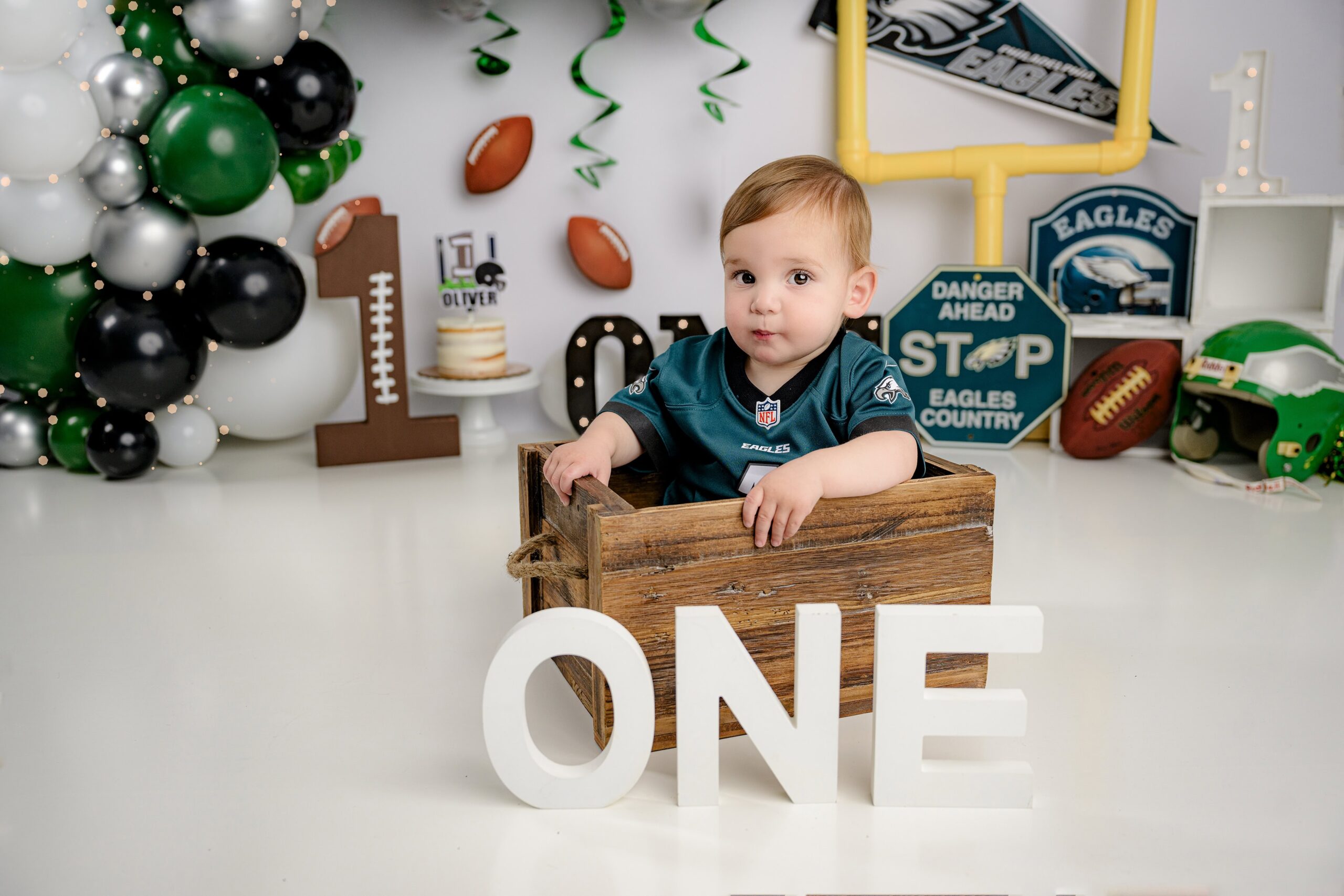 First birthday football cake smash session with a boy in an eagles jersey sitting in a crate