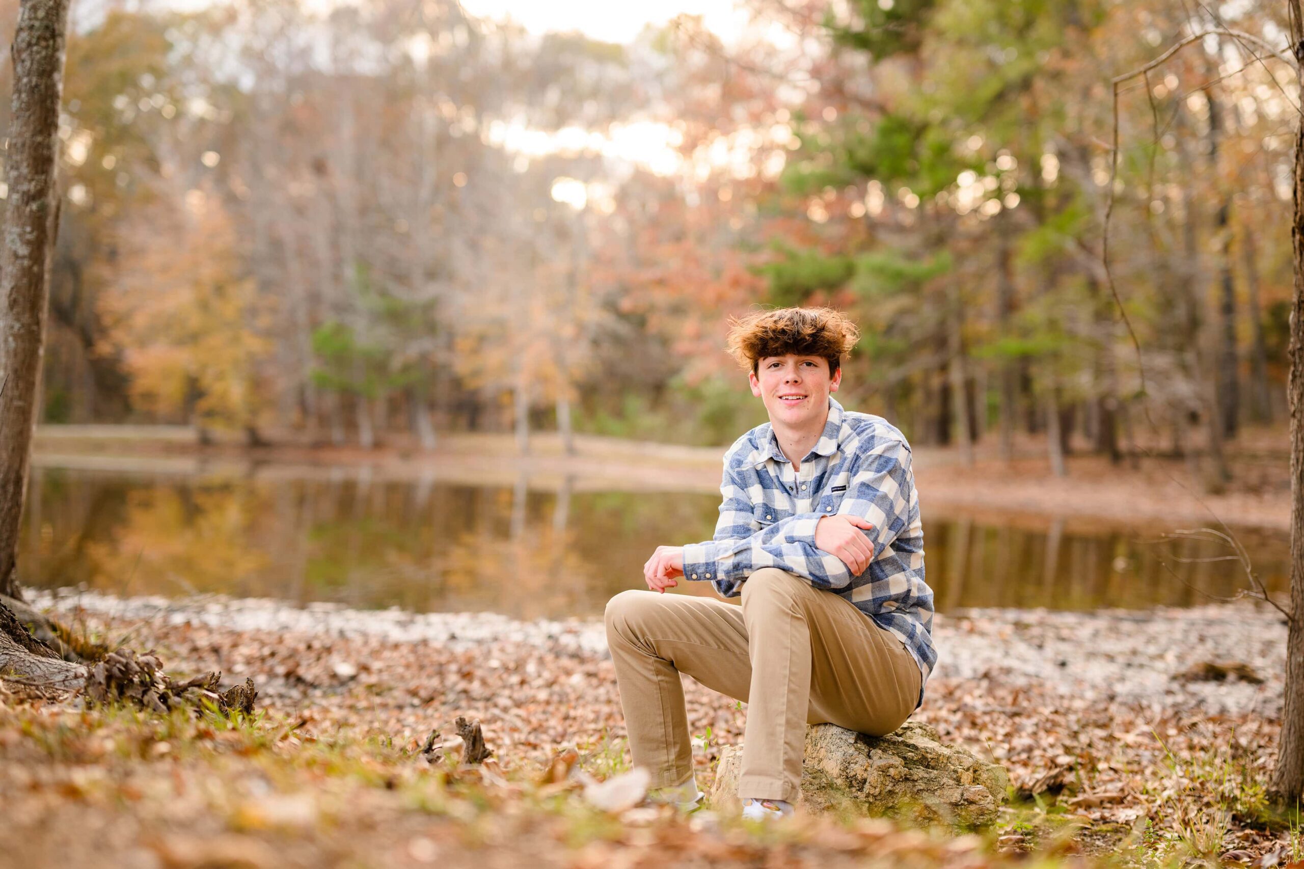 boy sitting in wooden surroundings wearing brown pants and a blue and white shirt