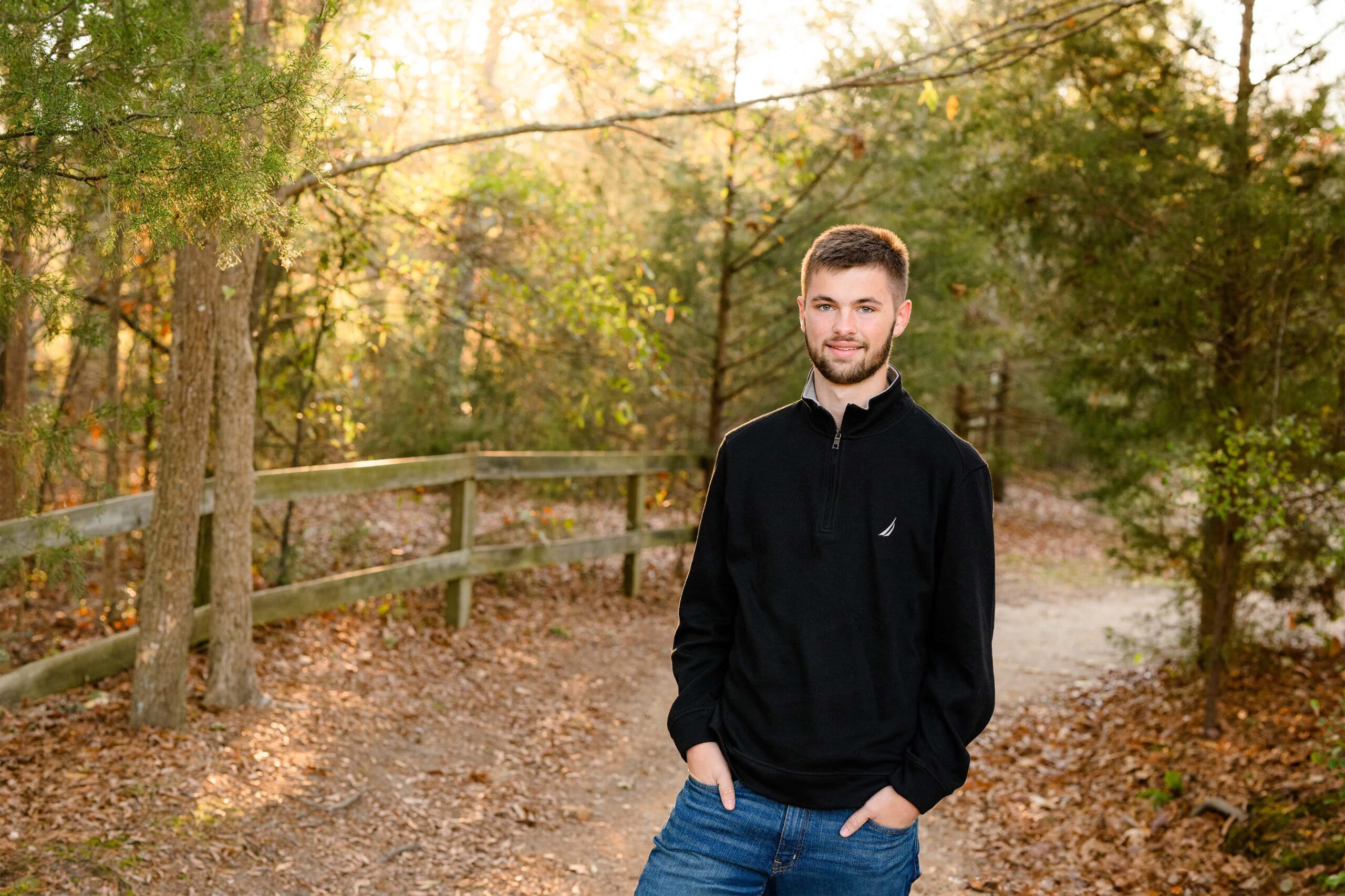 senior boy wearing a turtleneck black sweater and jeans in a wooden environment in golden light