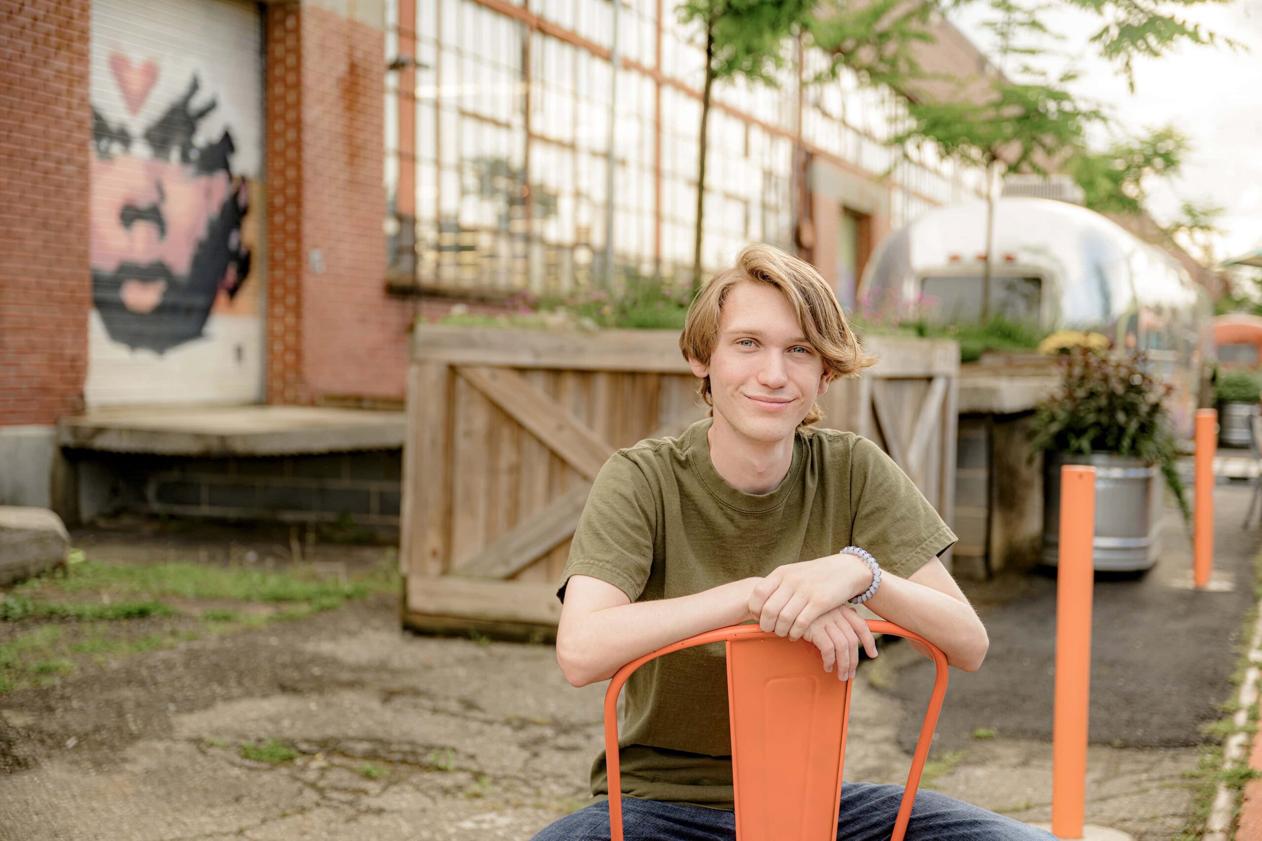 boy sitting backward in orange chair wearing a green t-shirt and jeans in an urban environment