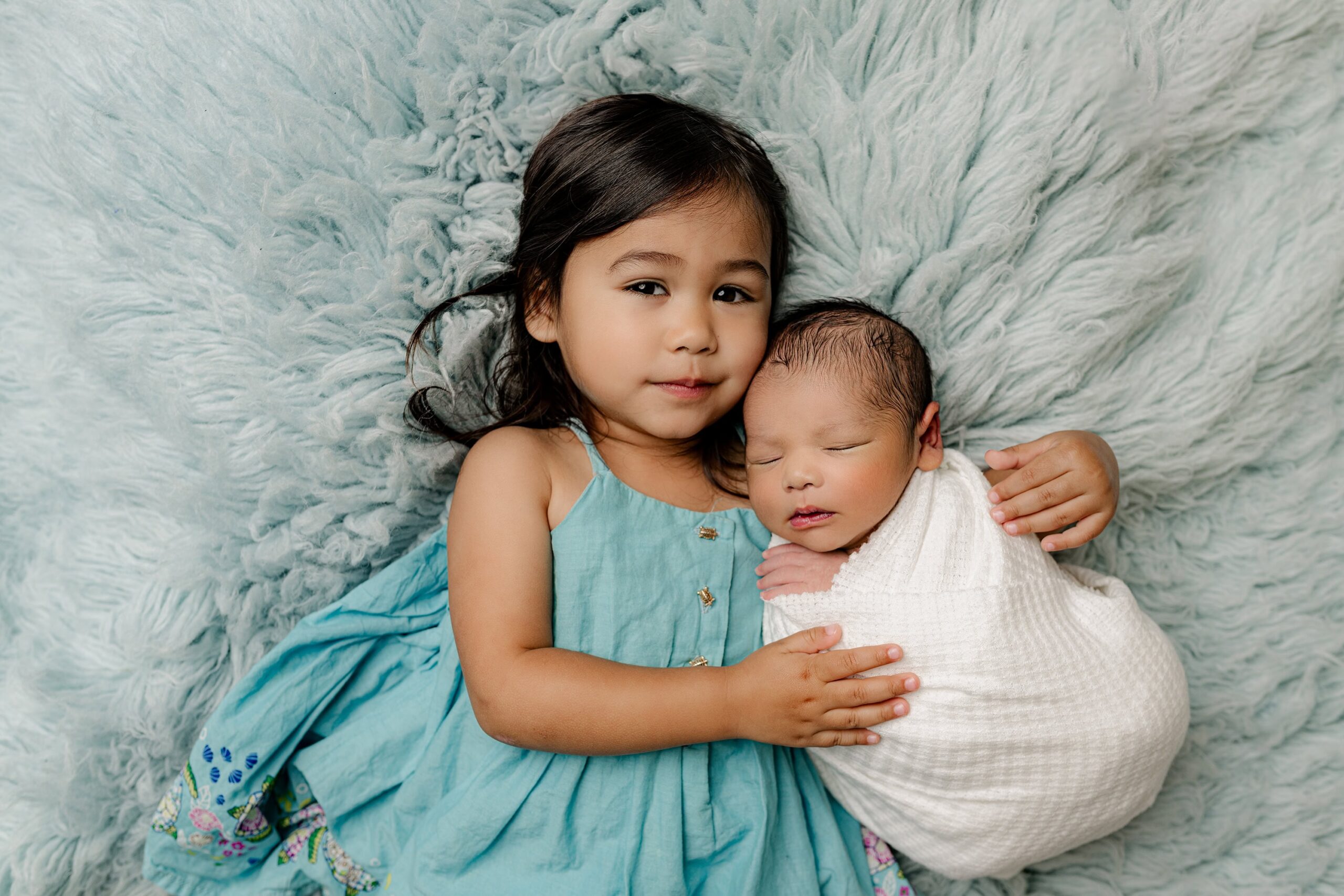 Charlotte area children in their family newborn session - with 3 year old daughter cuddling her newborn baby brother while lying on a blue fur