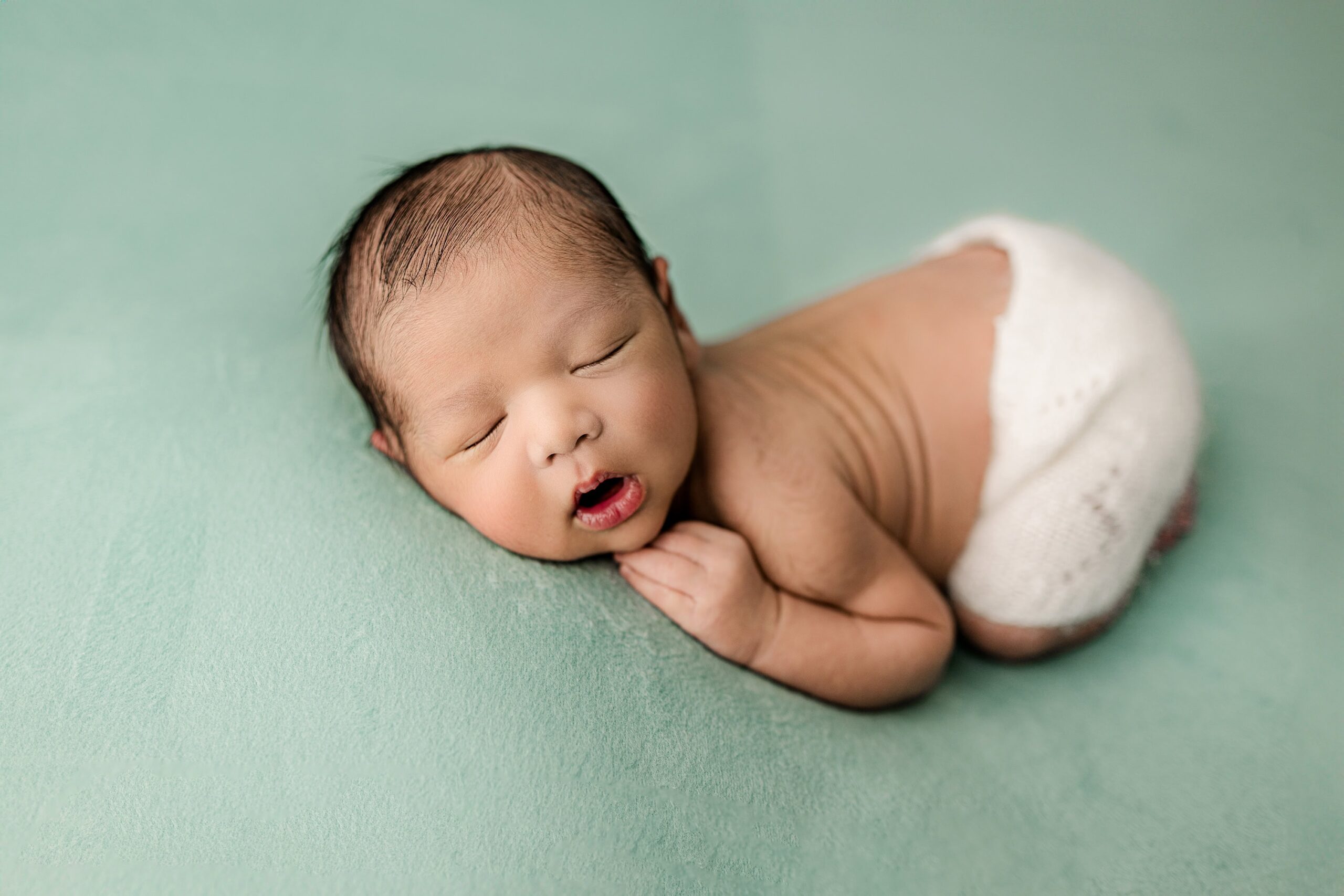 newborn boy wearing knit shorts lays in the bump up pose on a teal green background during their family newborn session in waxhaw, nc studio