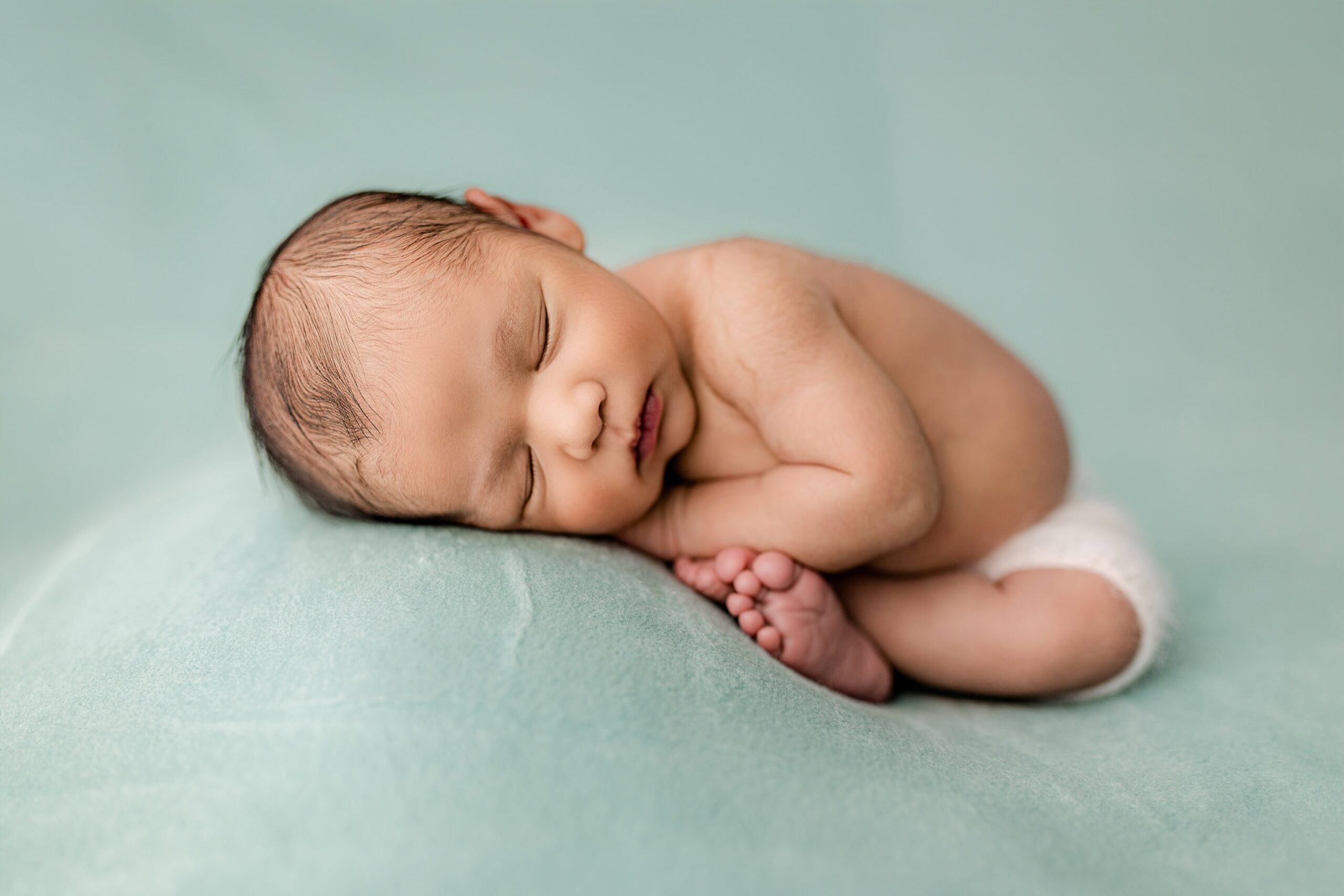 posed charlotte, nc newborn boy wearing white knit shorts on a teal green background