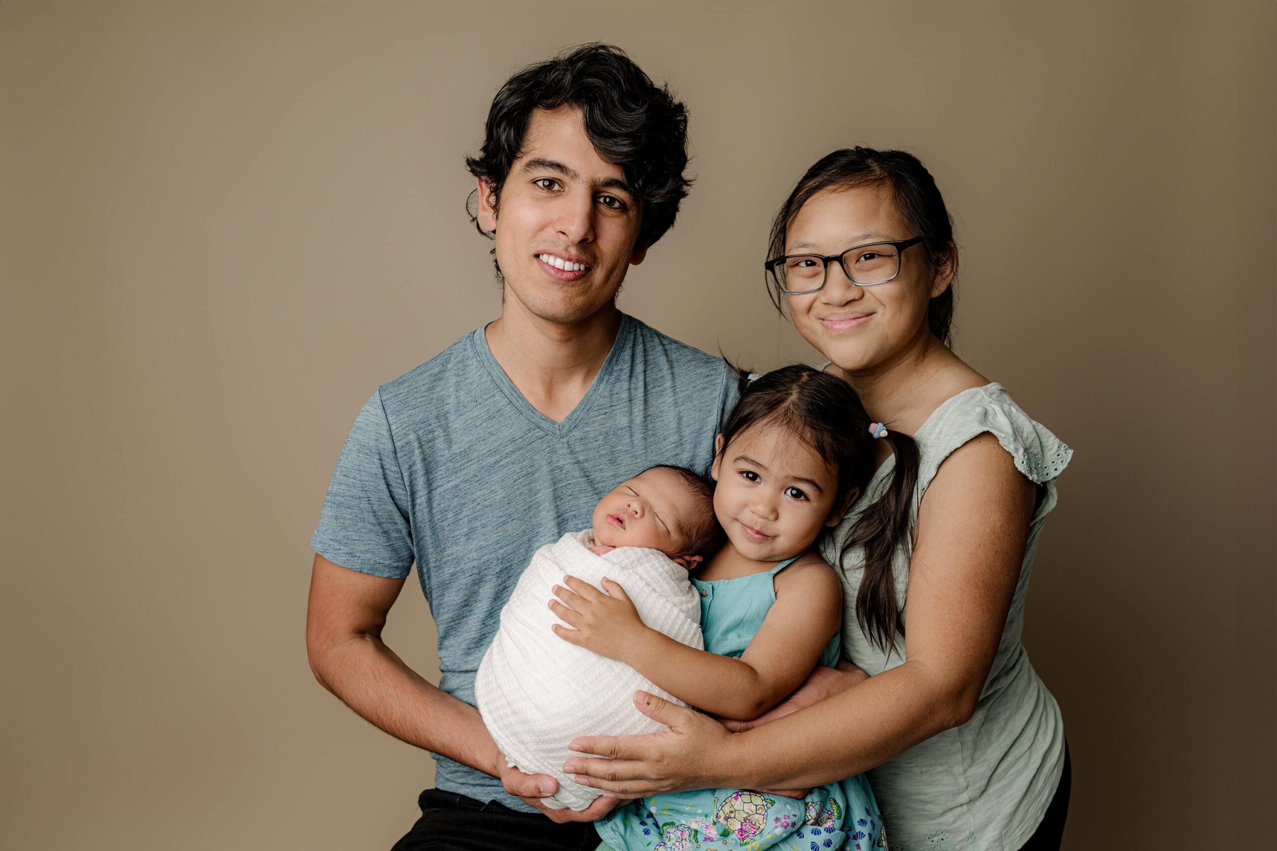 Family Newborn Session with a group of two parents and their two children together during holding their newborn baby wrapped in a white wrap in a charlotte area photography studio
