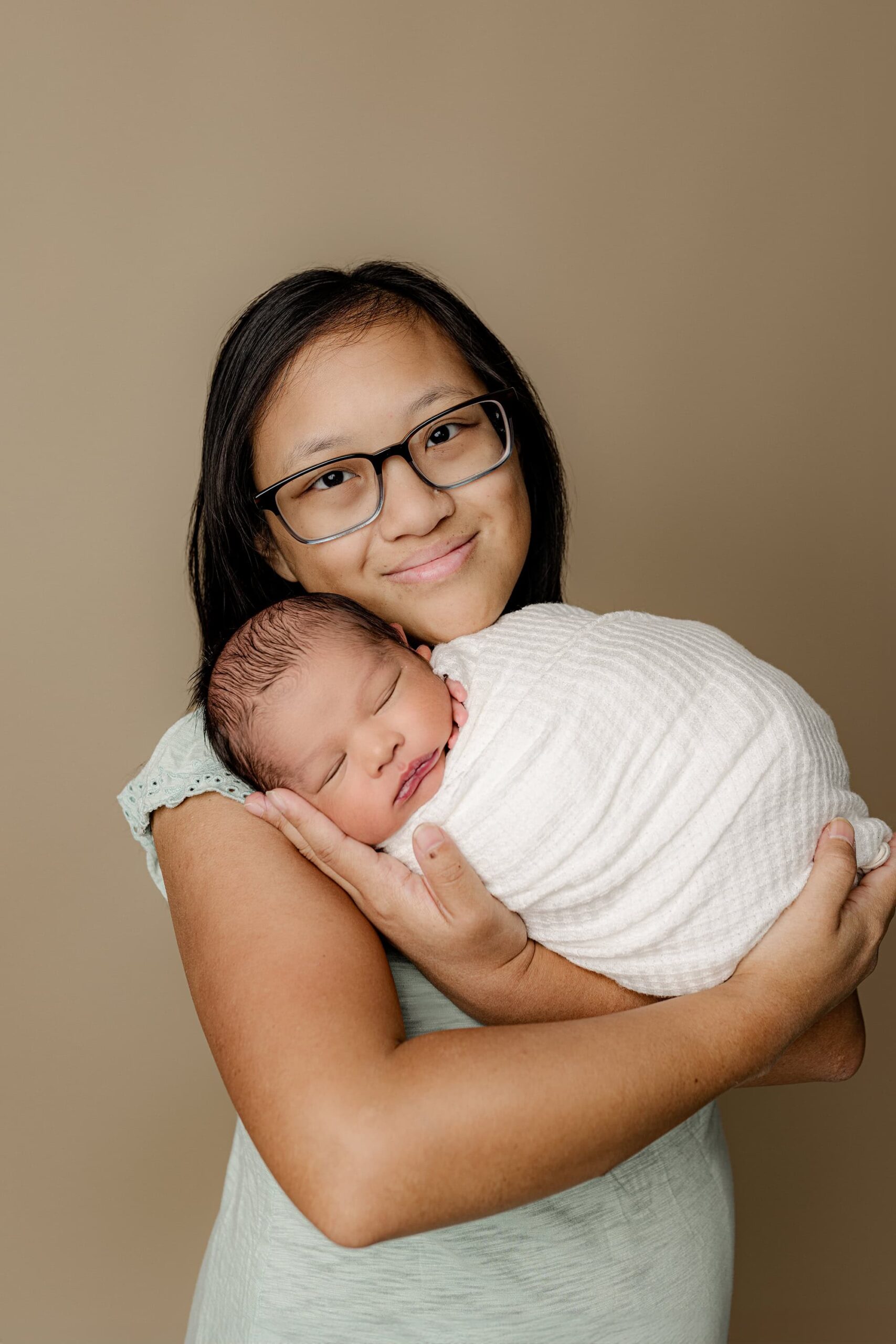 mother gently craddles her newborn son wrapped in white during their family newborn session in a waxhaw studio. mom is dressed in light blue and the newborn is wrapped in white.
