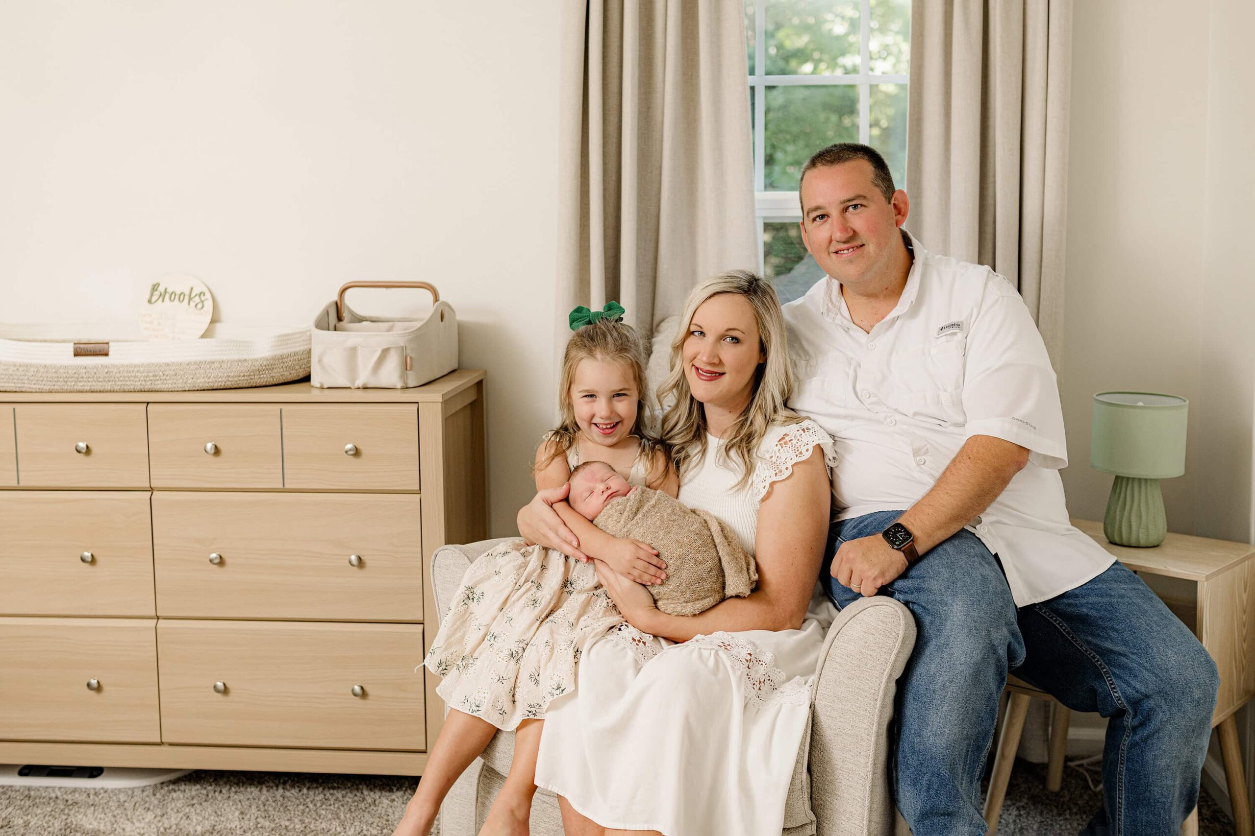 posed family photo of a family of four perfectly put together as they sit in a chair in their newborn's indian land sc nursery