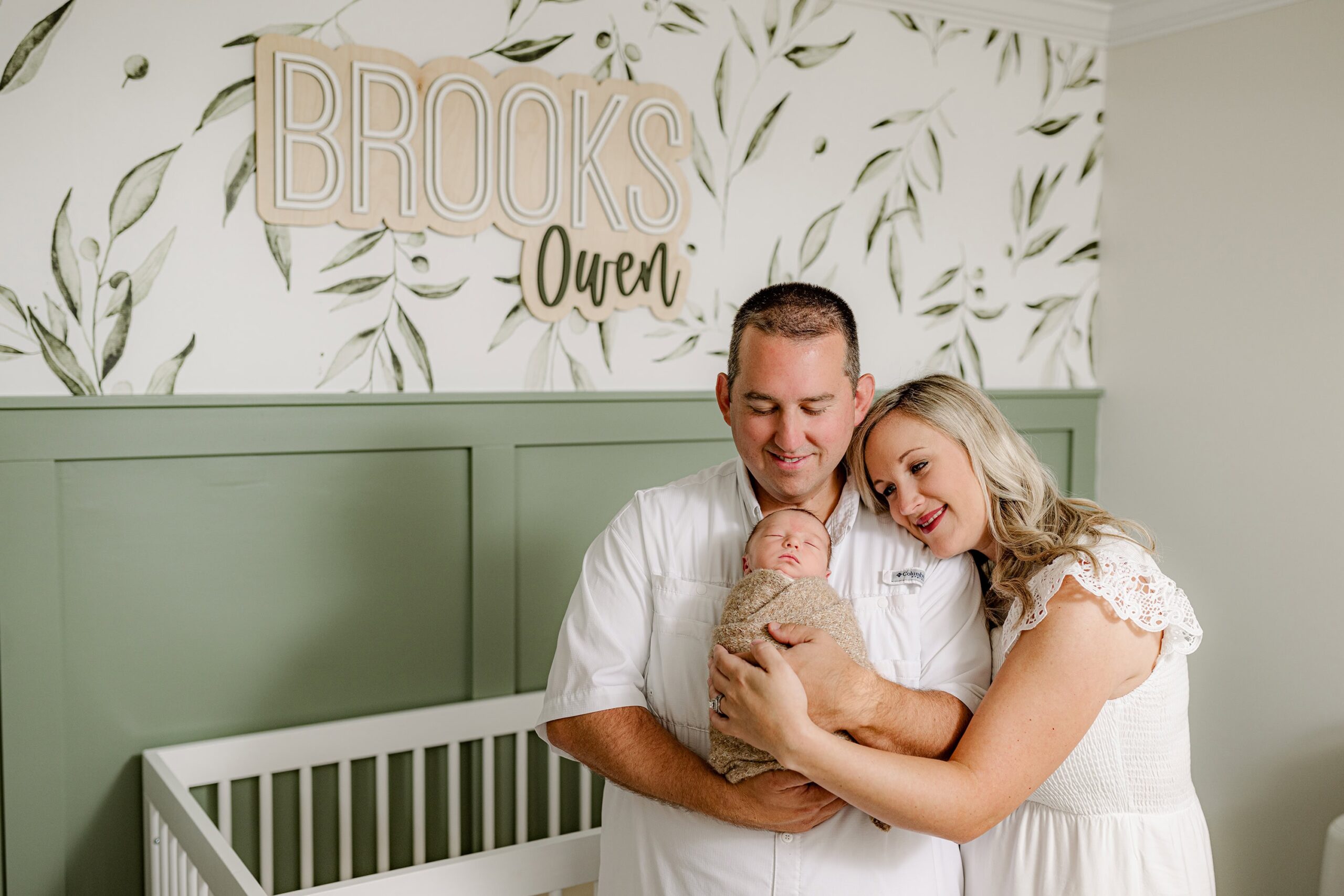 Mother and father together while holding their newborn son in his natural nursery during their lifestyle newborn session