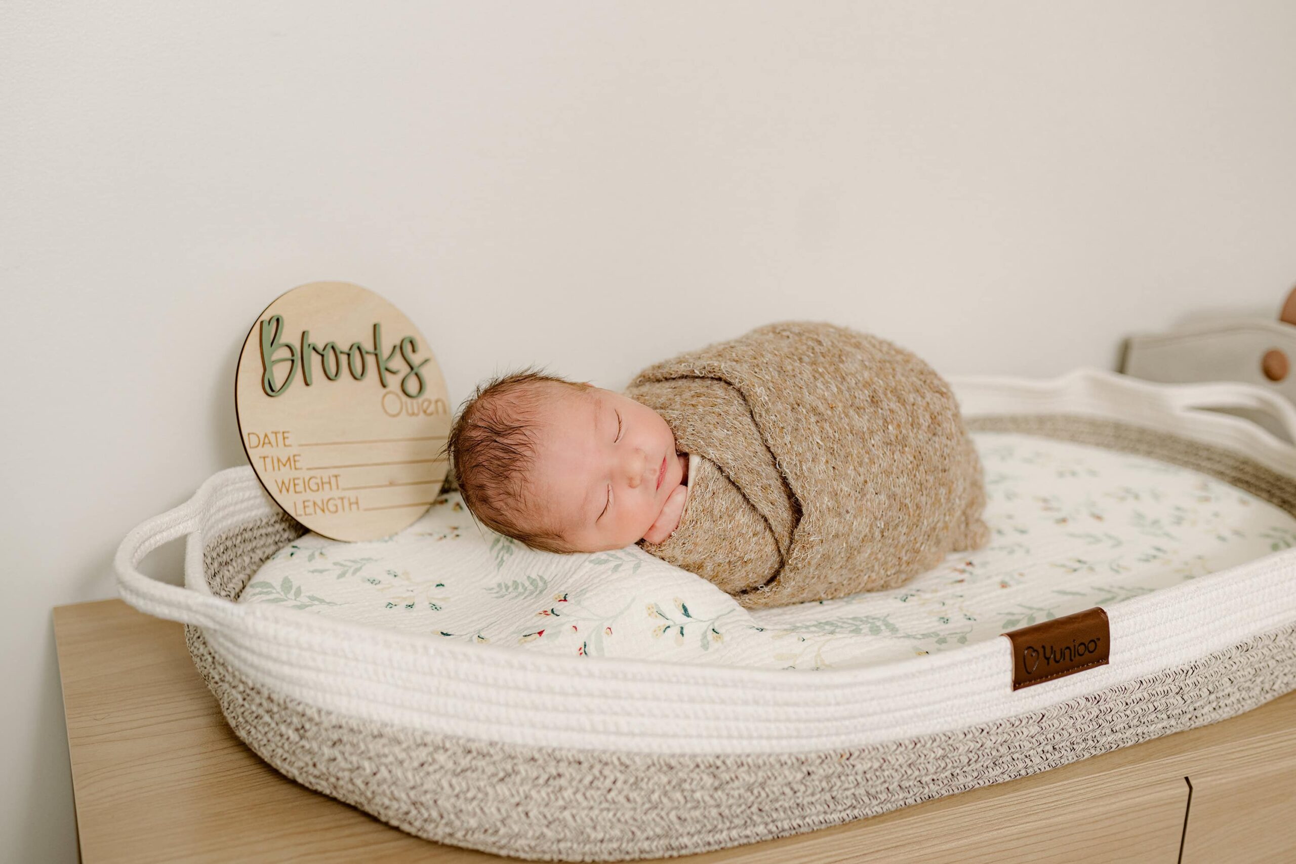 newborn son lays in basket with his wooden name plate beside him