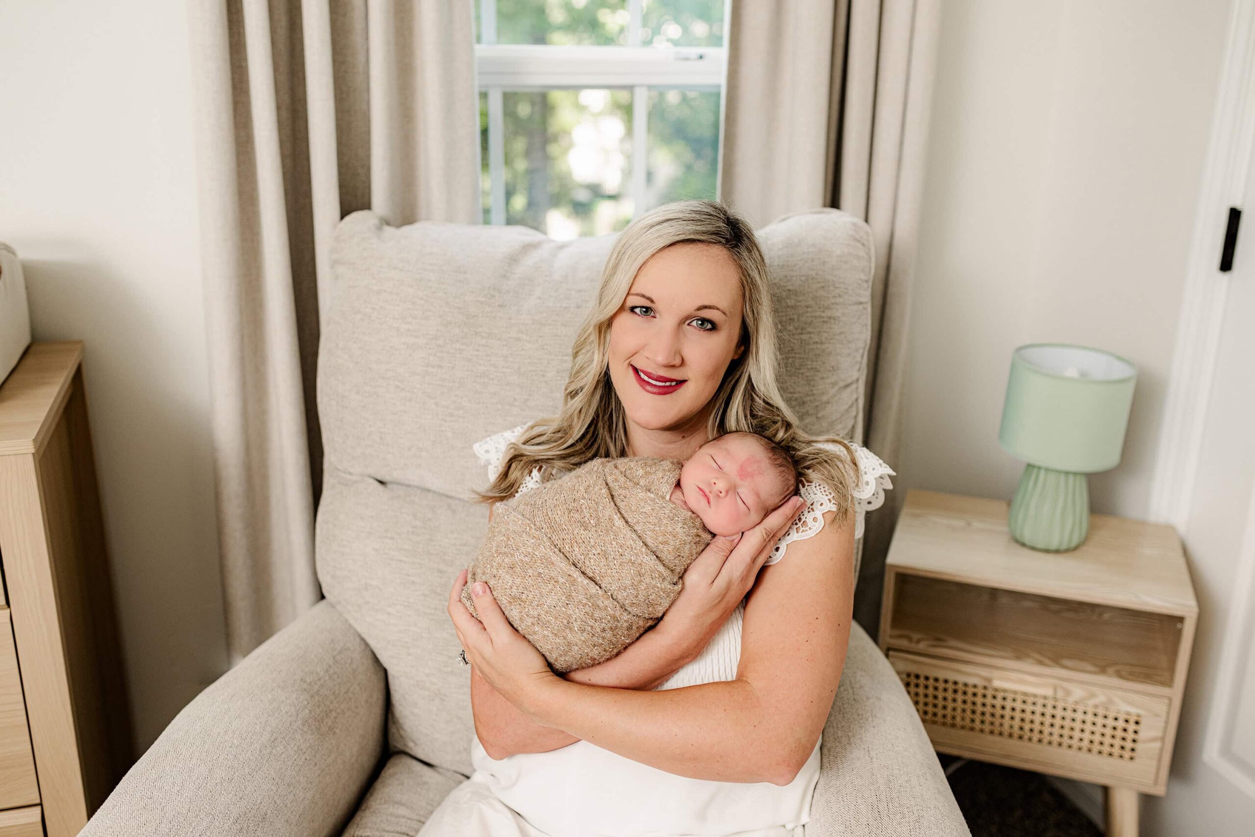 baby wrapped in brown is held by his mom dressed in cream sitting in a chair during his lifestyle newborn session