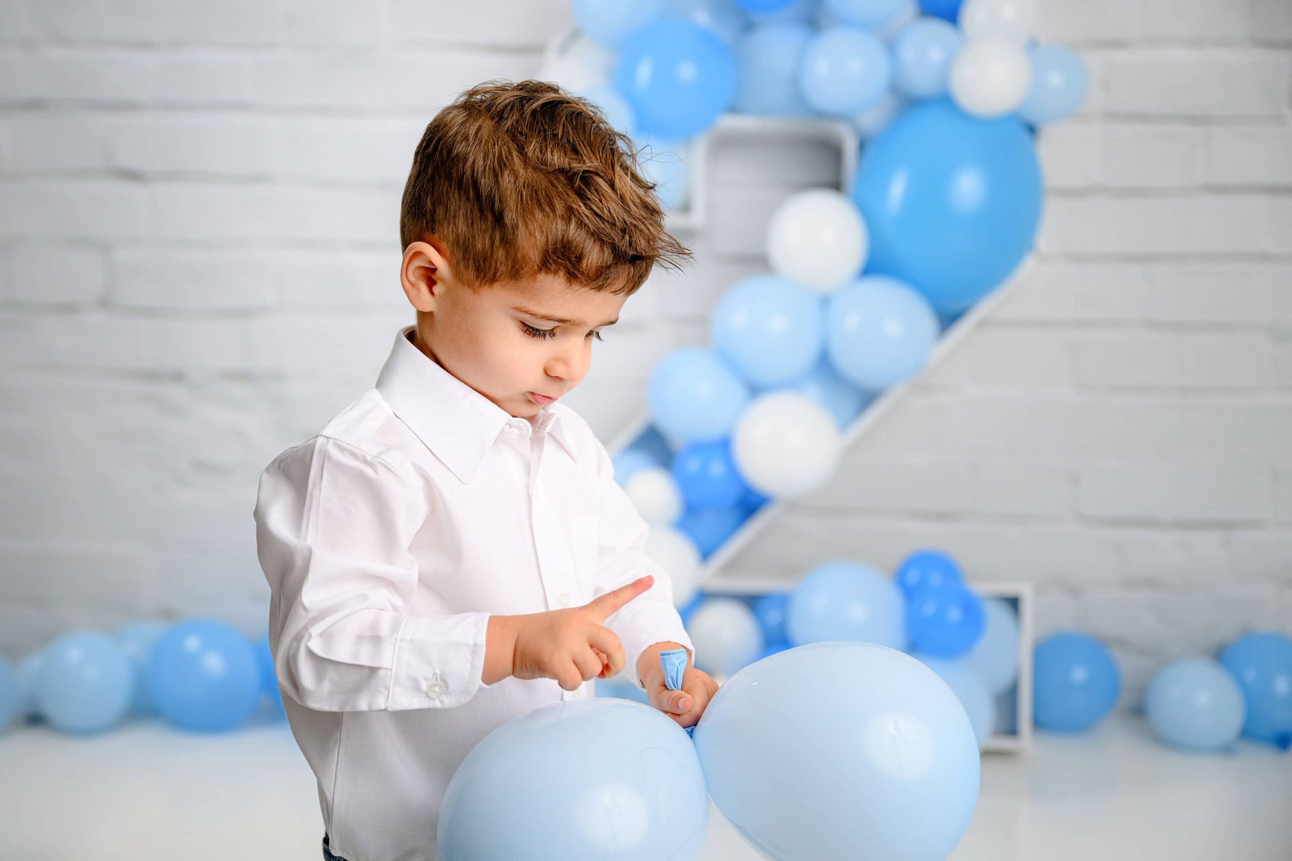 little boy dressed in a white shirt plays with balloons during his Two-year-old Milestone photography session