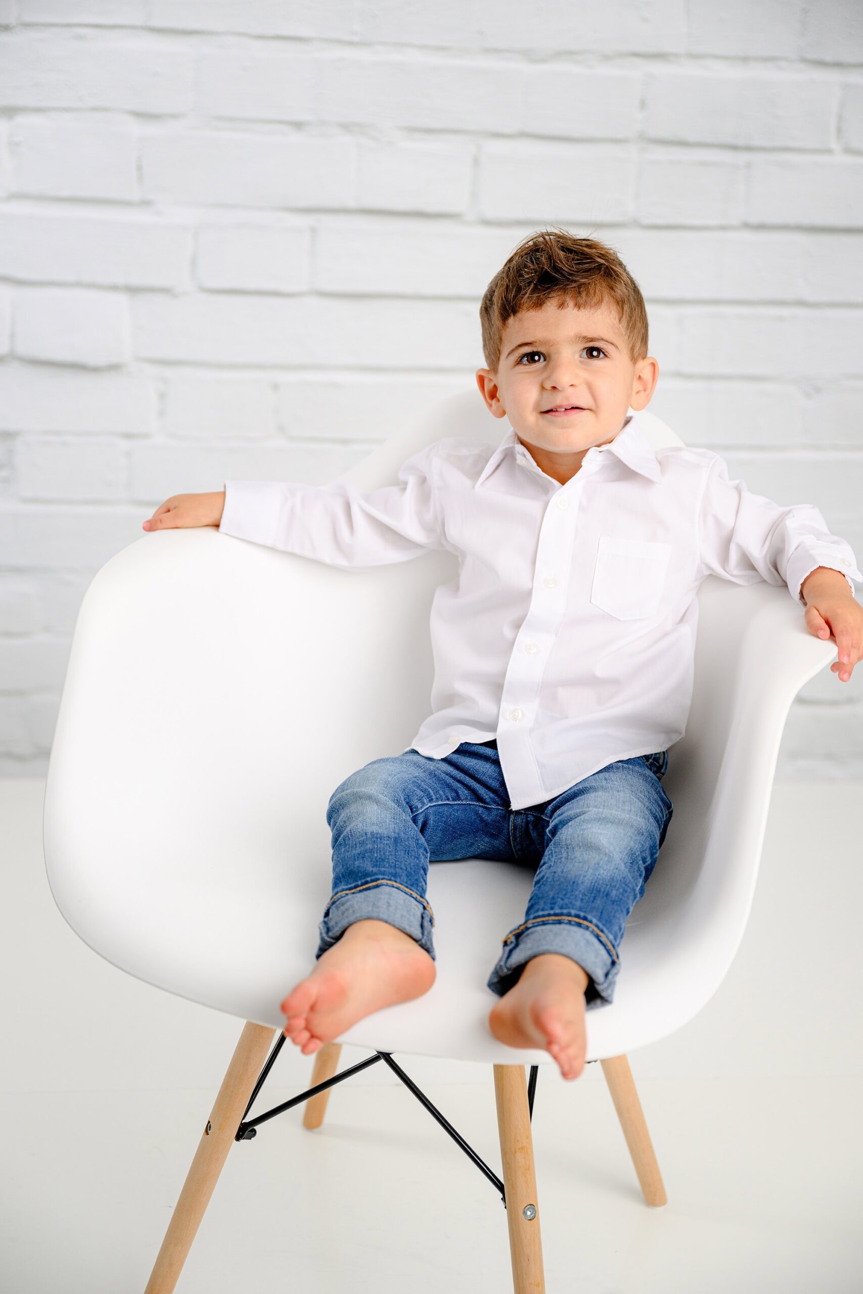 Boy wearing jeans and white shirt sitting in his chair during his two-year-old milestone session