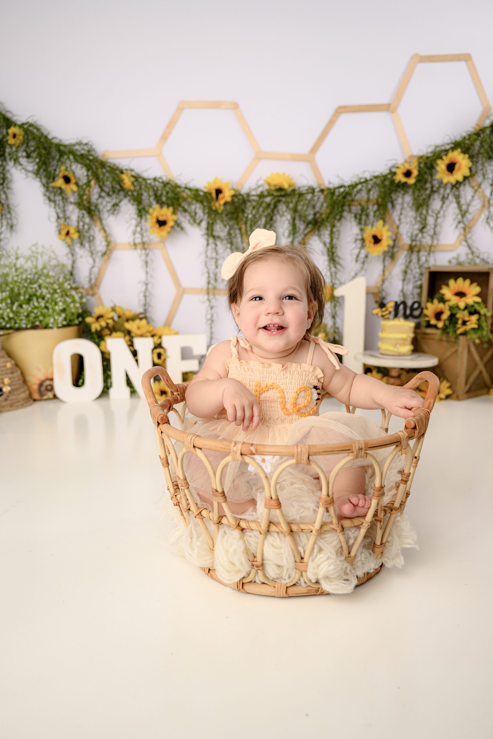 one year old little girl laughing at mommy and photographer while sitting in a basket during her milestone session