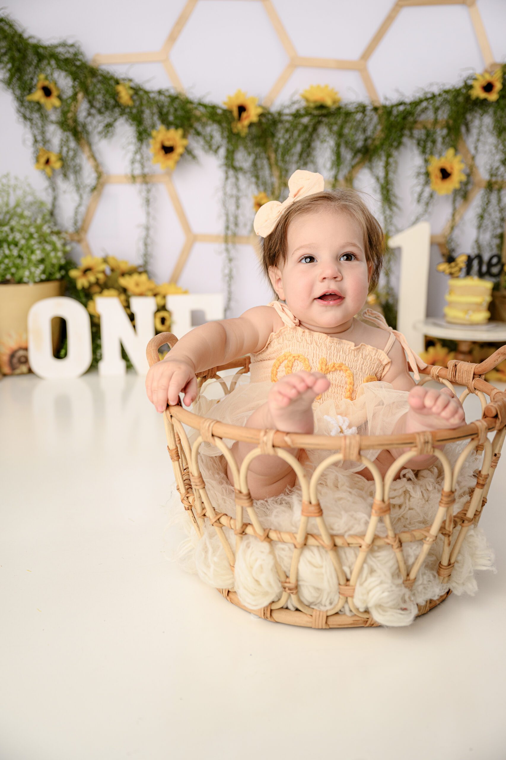one year old little girl sitting in a basket with her feet popping out over the top during her milestone session