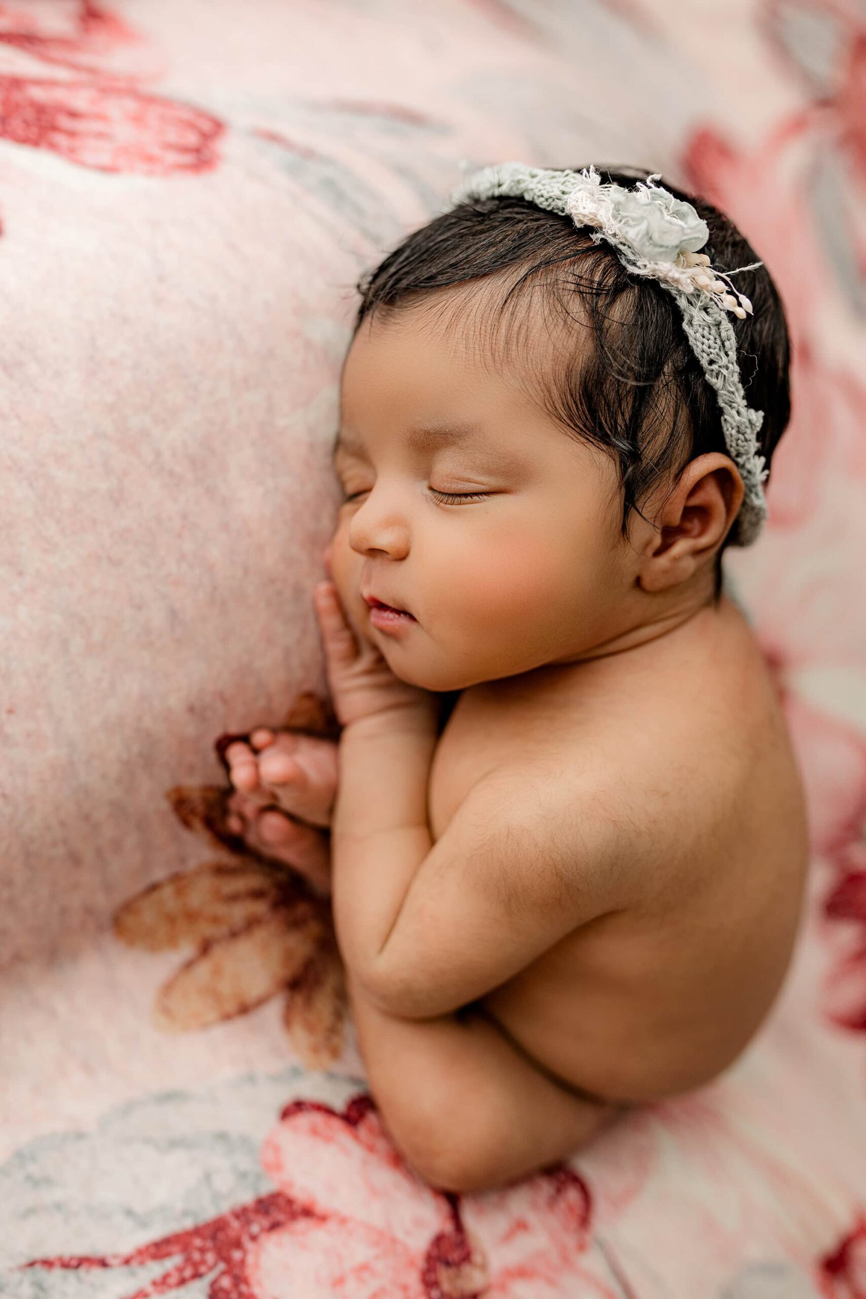 An overhead shot of the baby girl in the same taco position, showcasing her perfect profile and long, fluttery eyelashes. The teal and pink floral newborn photo backdrop adds a soft, vibrant touch to the serene moment.