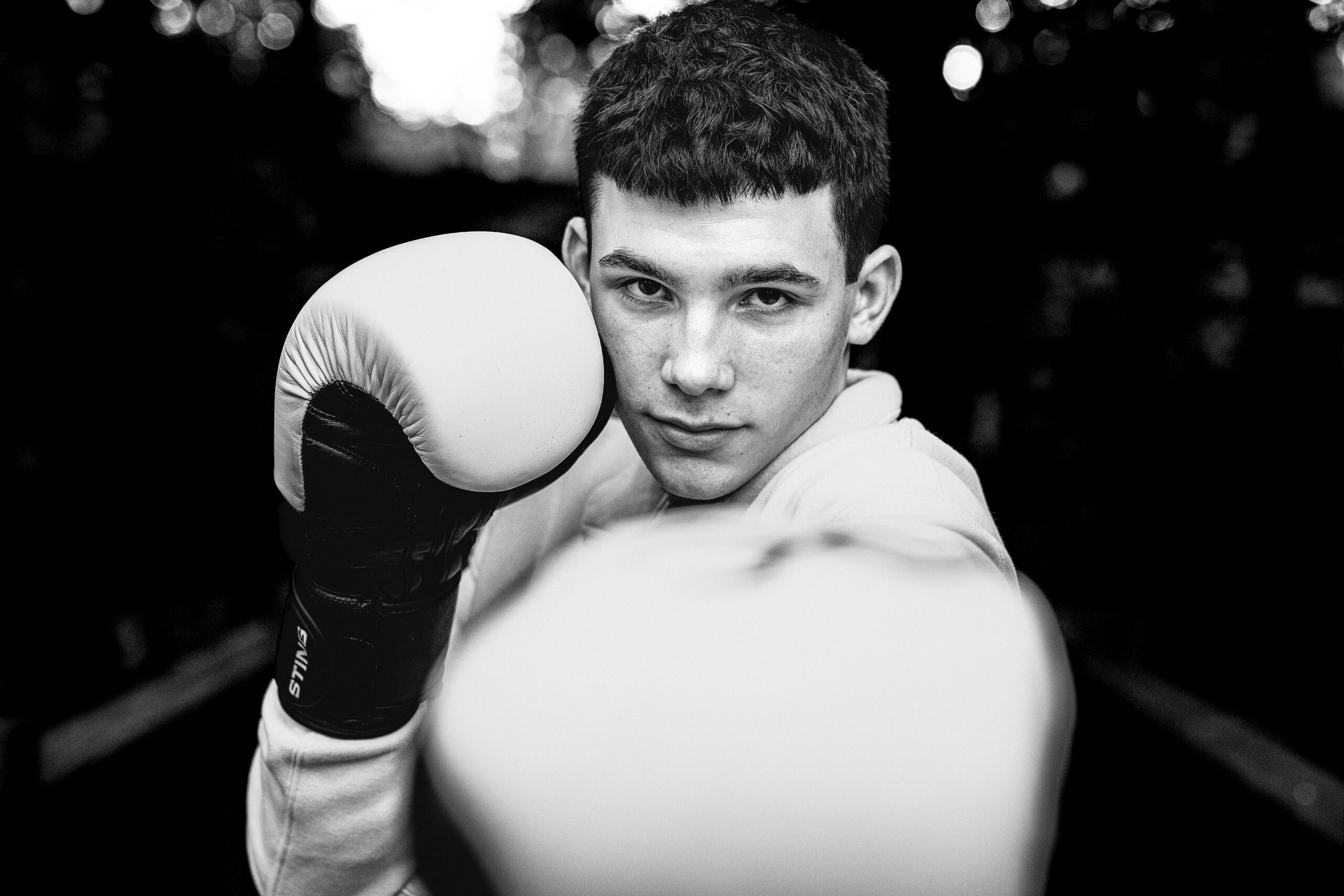 senior boy standing in a power pose wearing his boxing gloves highlighting his love of his sport with a personalized meaningful senior session prop