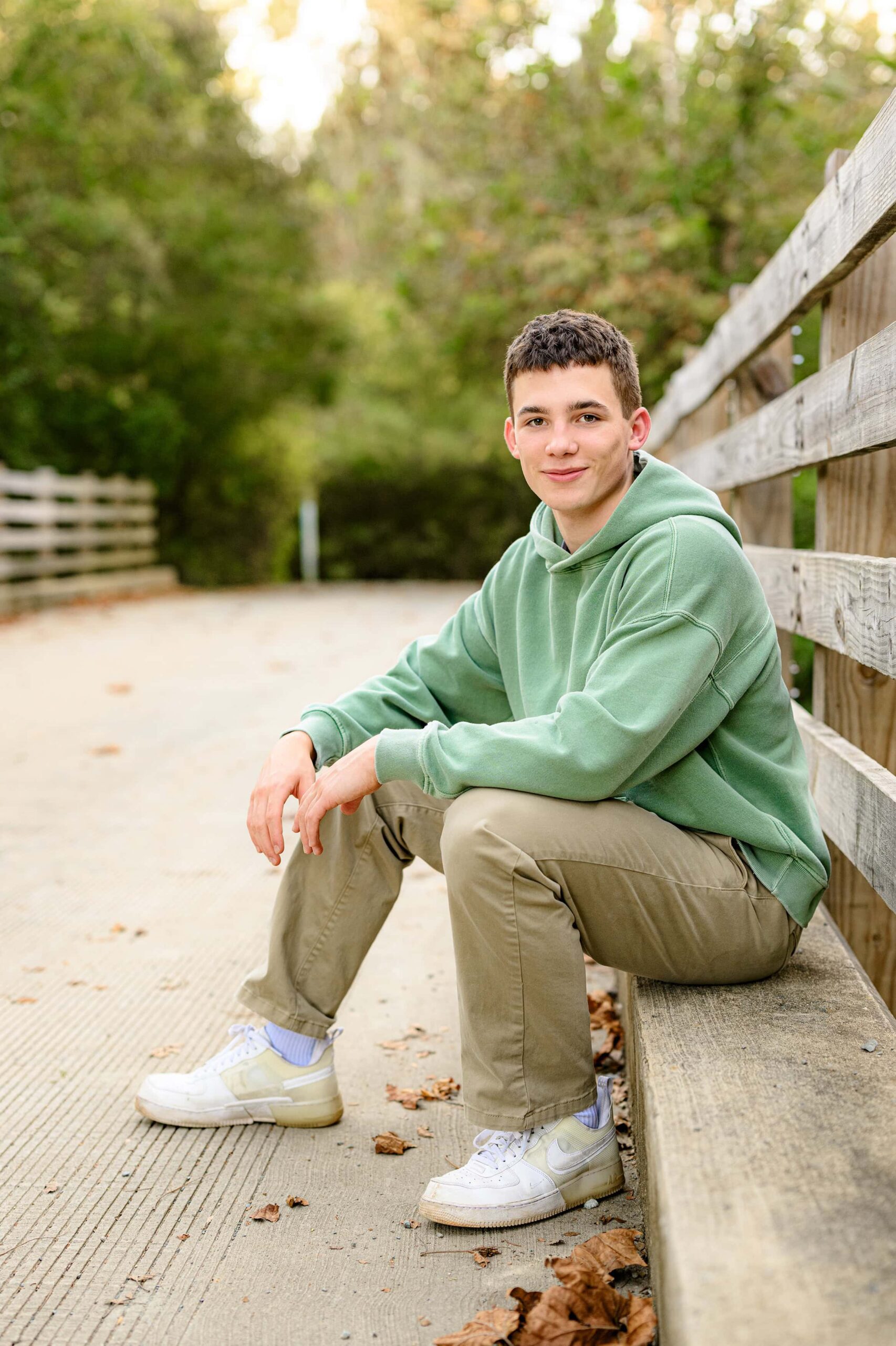 Senior boy sits on curb dressed in green shirt and brown pants