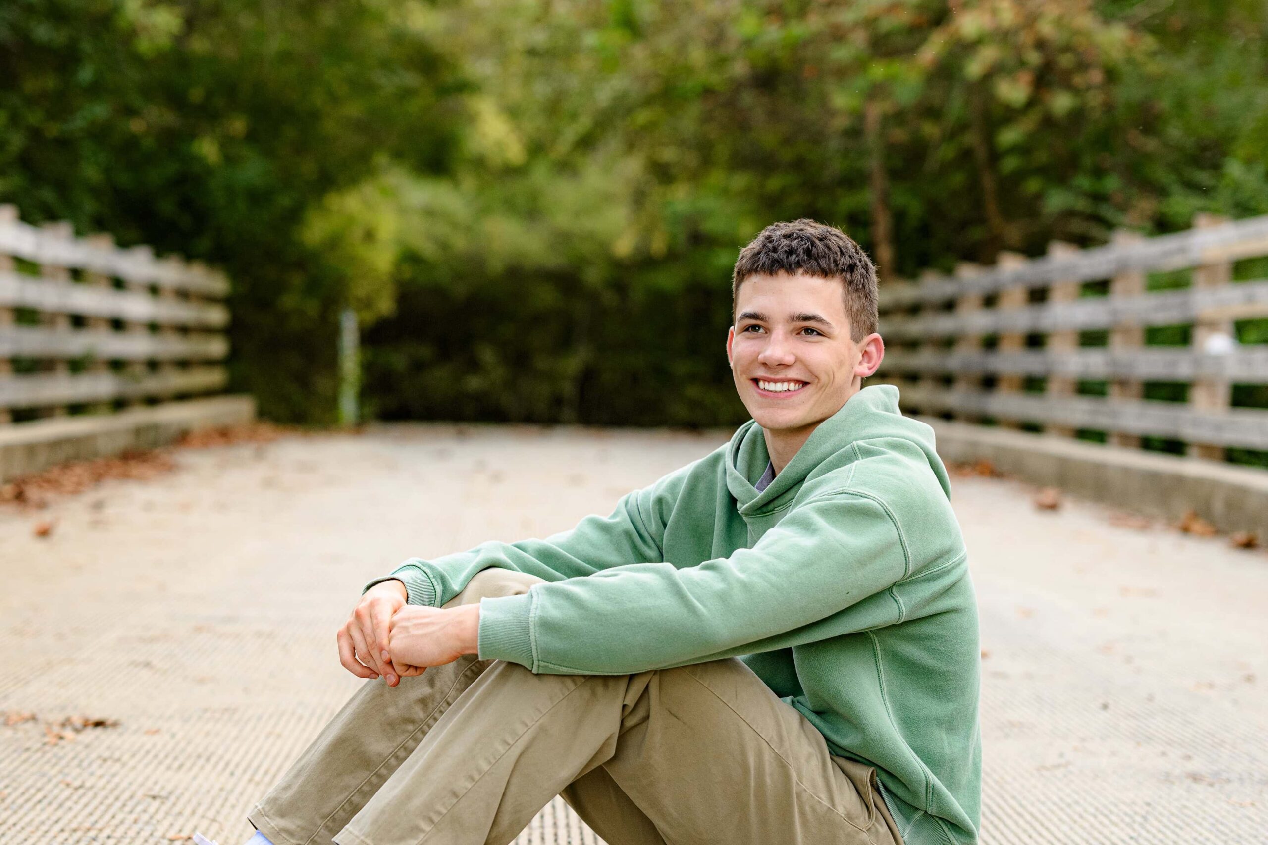 wearing a green shirt and smiling a senior boy sits looking off camera