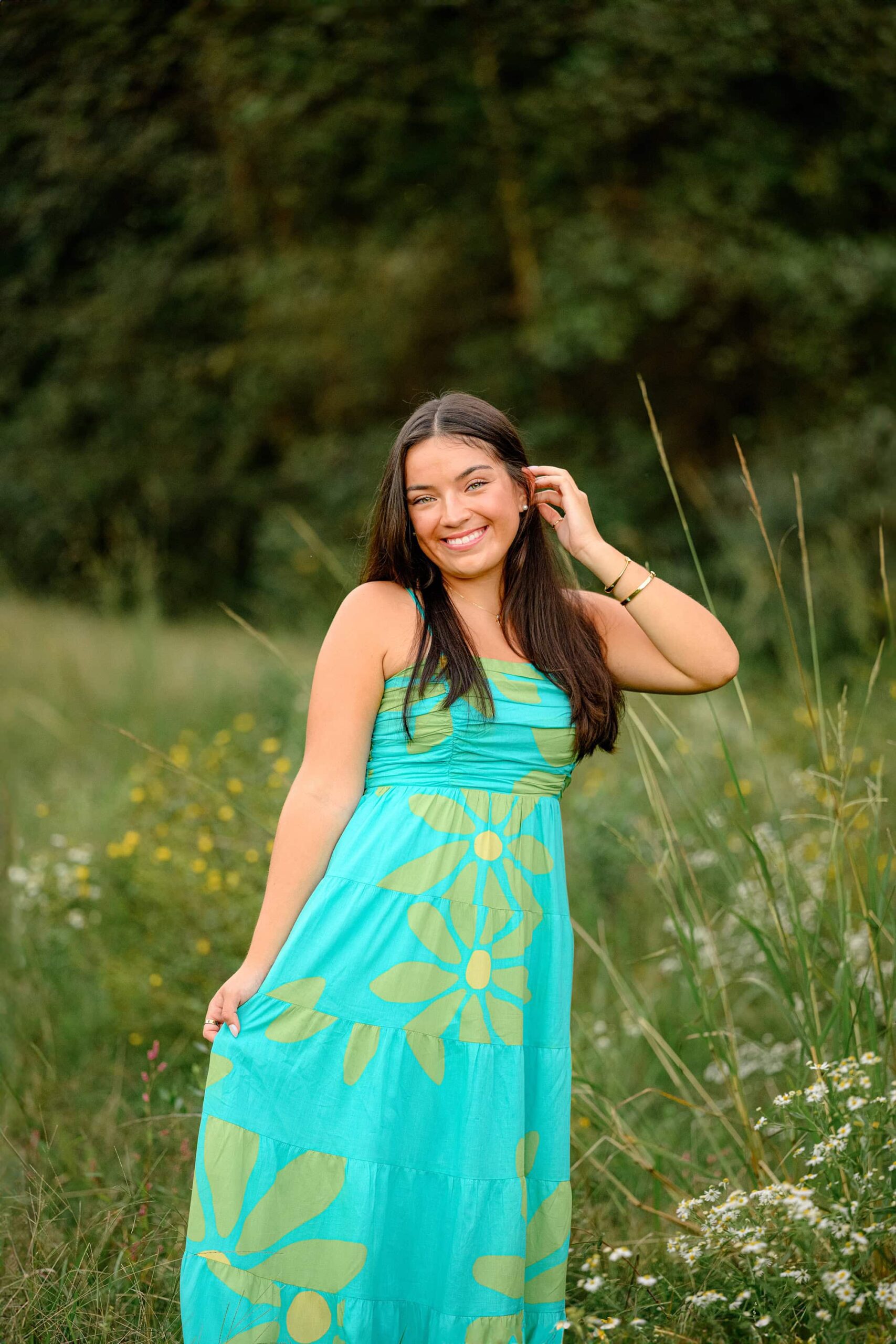 senior girl holding her dress standing in a field tucking her hair behind her ear during her perfect portrait photoshoot session in waxhaw, nc
