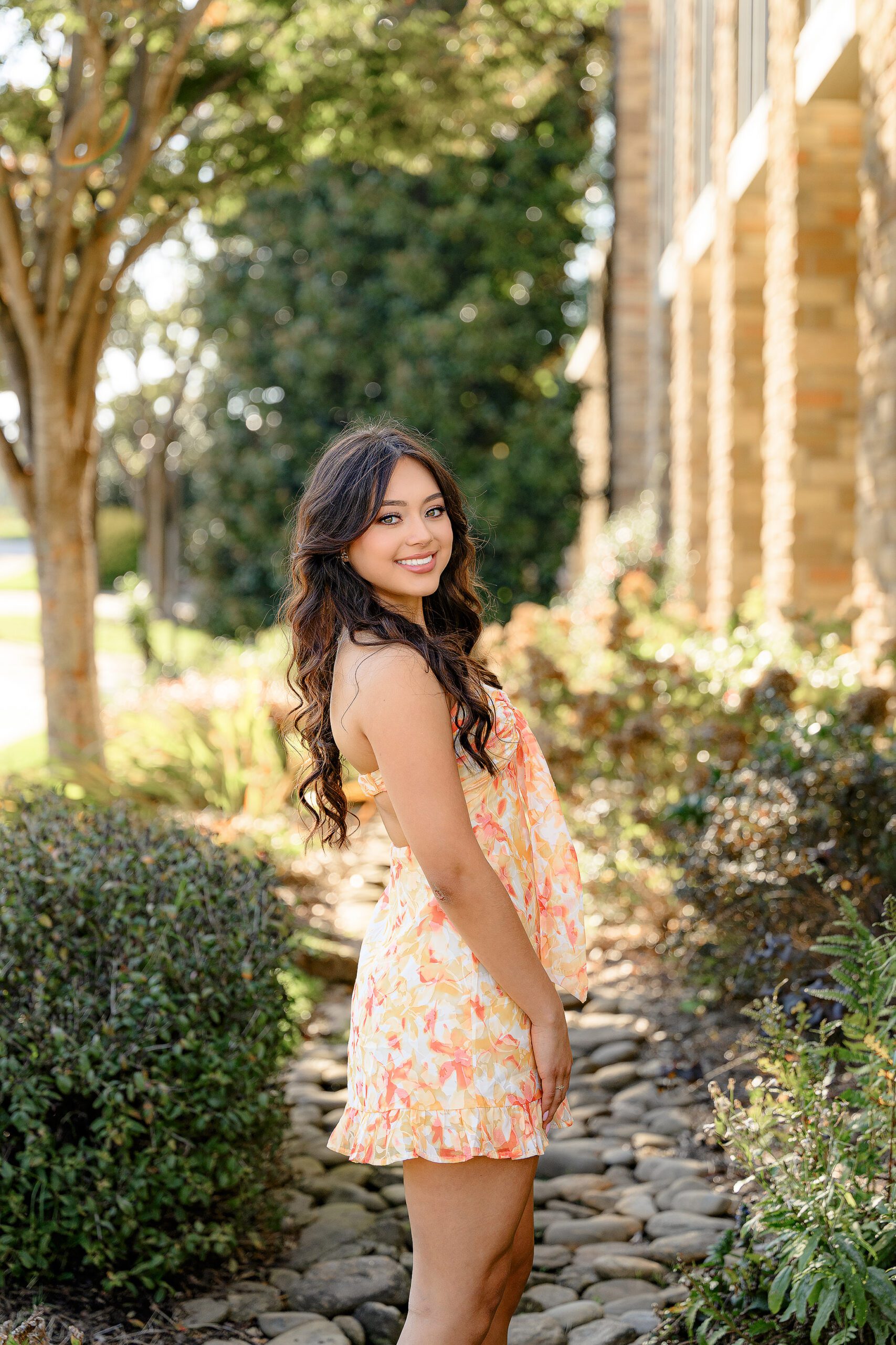 Class of 2025 Senior looked over her shoulder while dressed in an orange and yellow romper