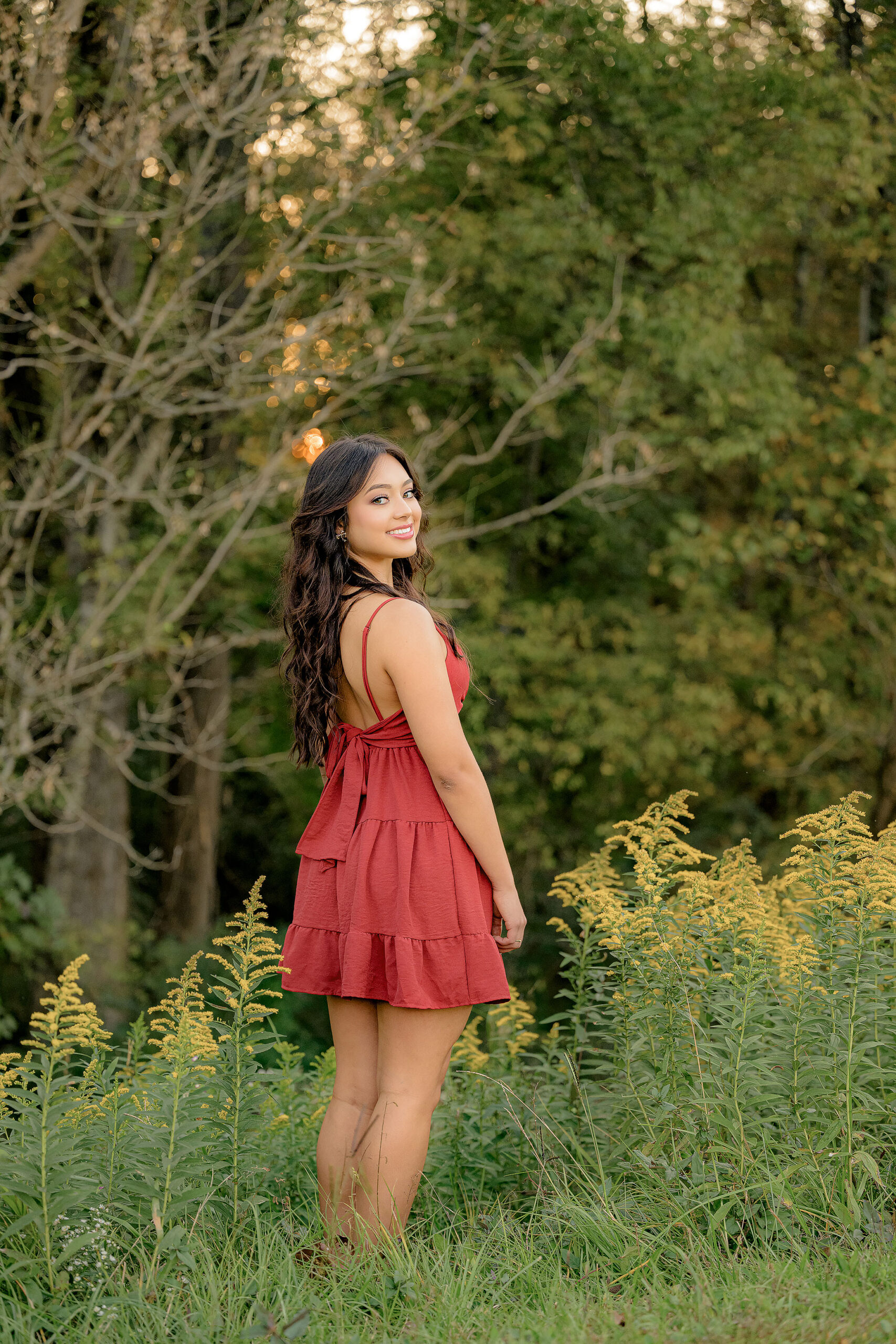 Senior girl looks casually over her shoulder whilst surrounded in fall colors and dressed in a red dress