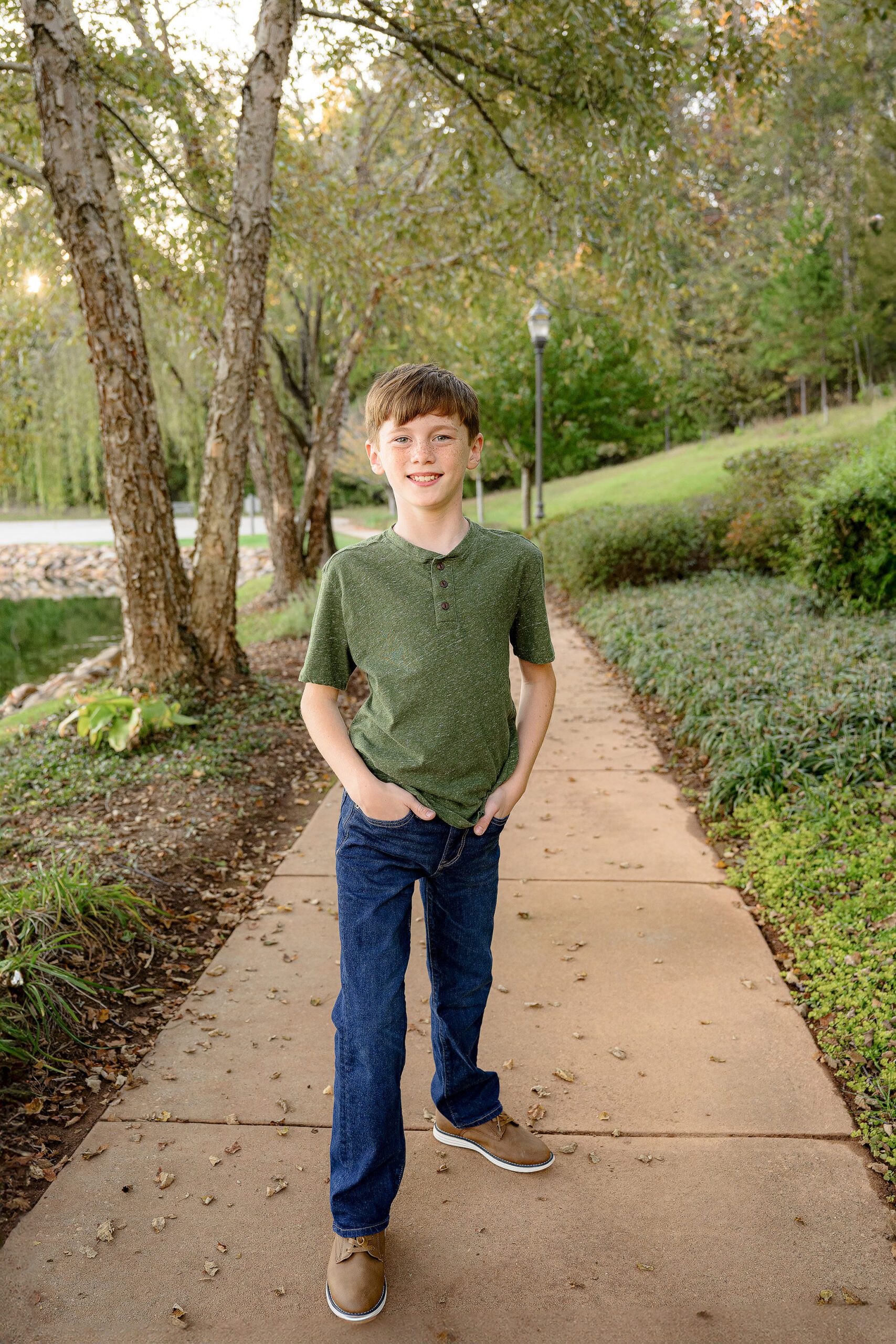 9 year old boy stands with his hands in his pockets wearing a green shirt