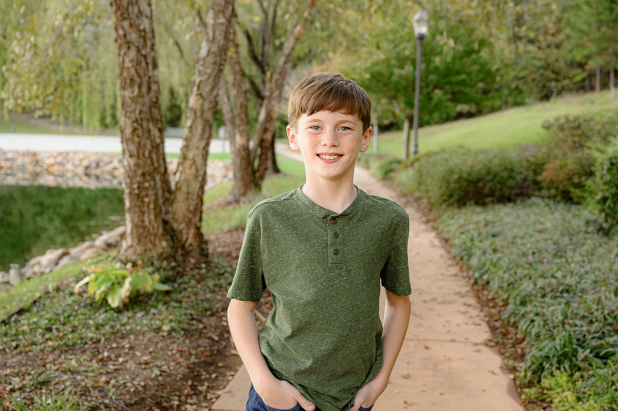 9 year old boy stands with his hands in his pockets wearing a green shirt