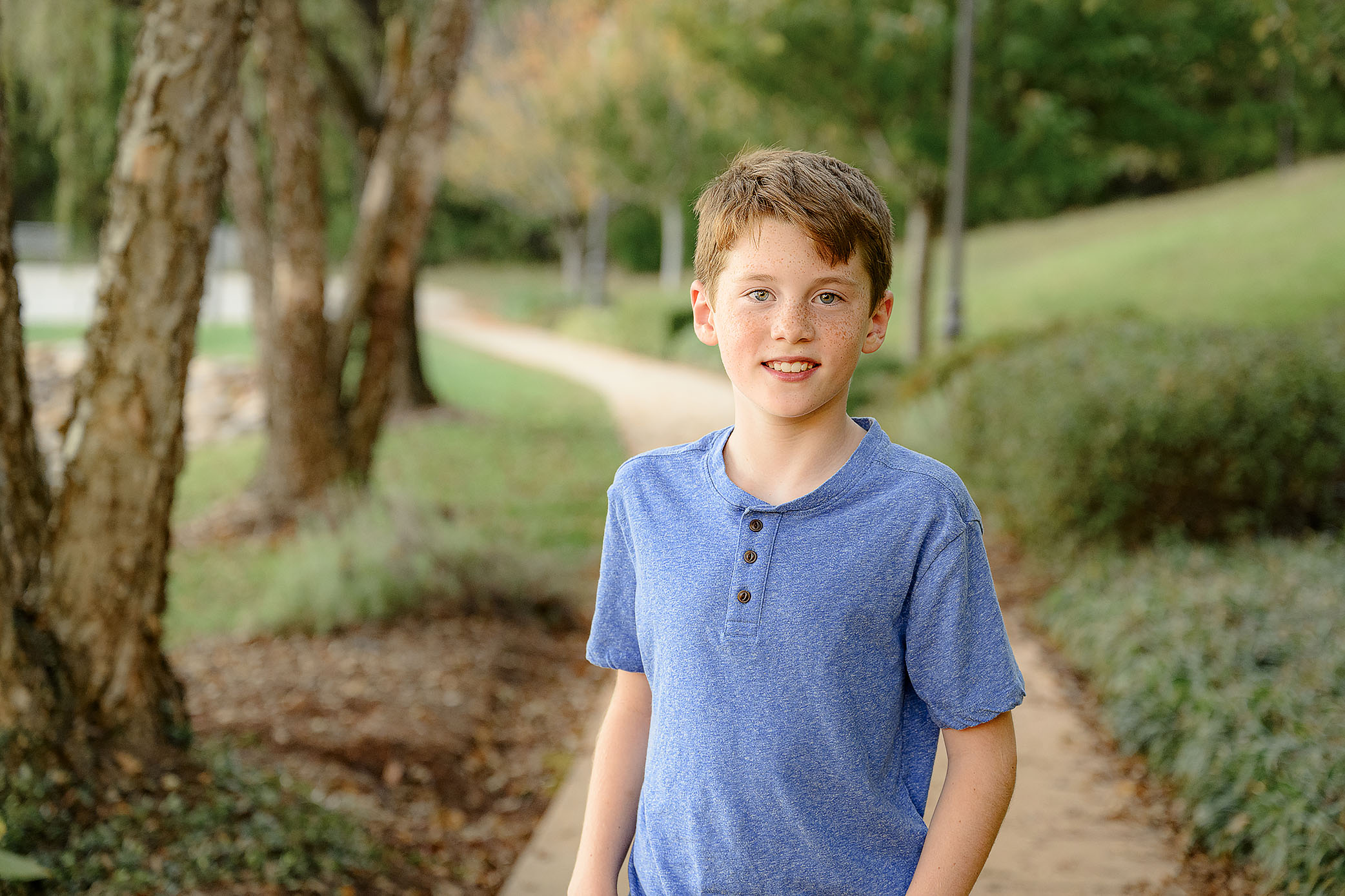 9 year old boy stands with his hands in his pockets wearing a blue shirt