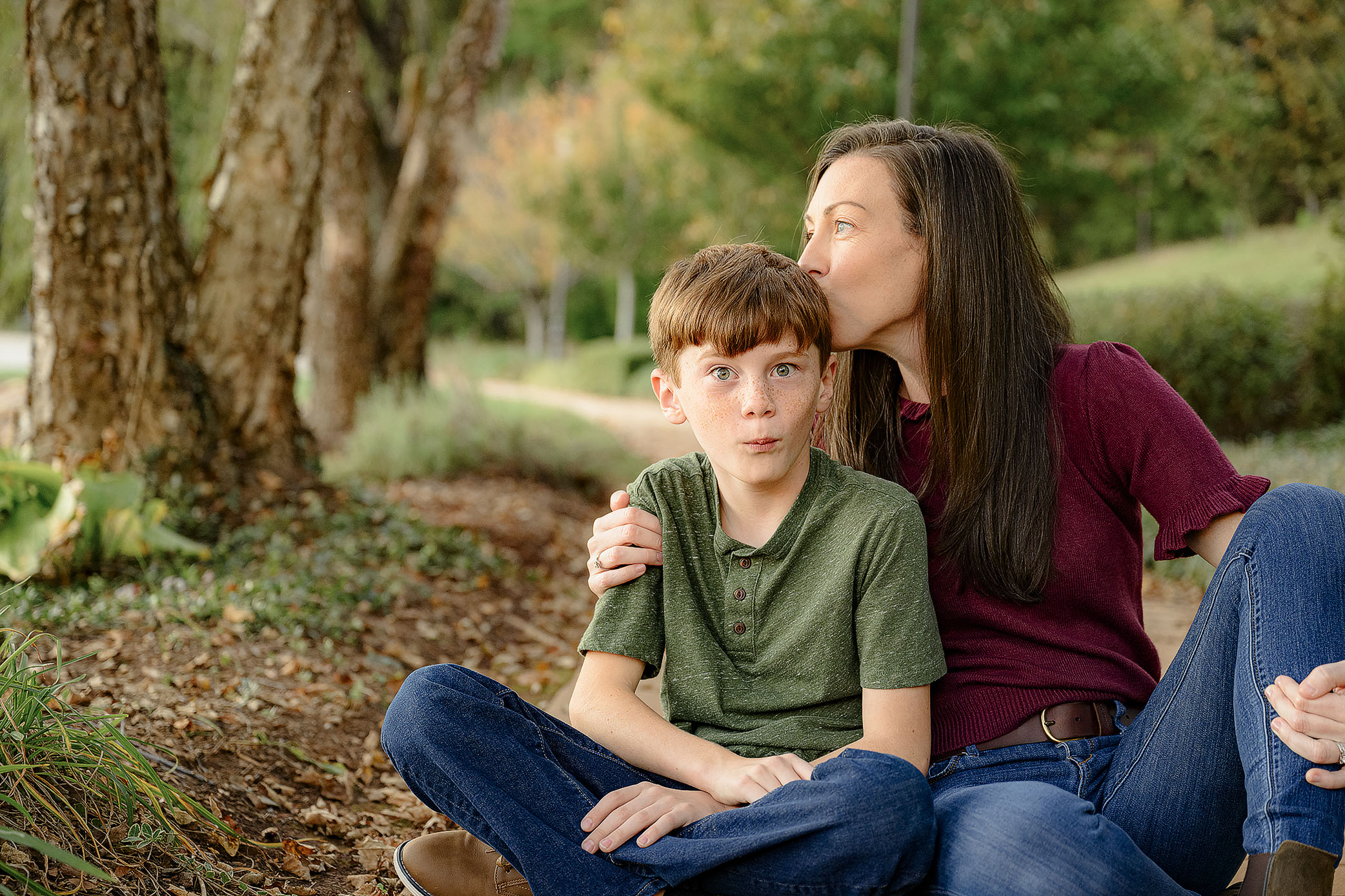 mom dressed in burgundy kisses the top of her 9 year old sons who is dressed in greens head