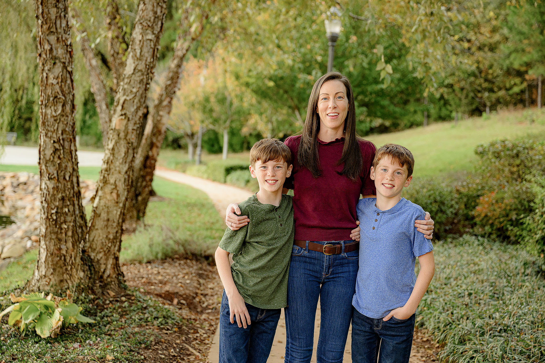 mom standing wearing a burgundy sweater with her arms around her twin boys each wearing blue or green shirts