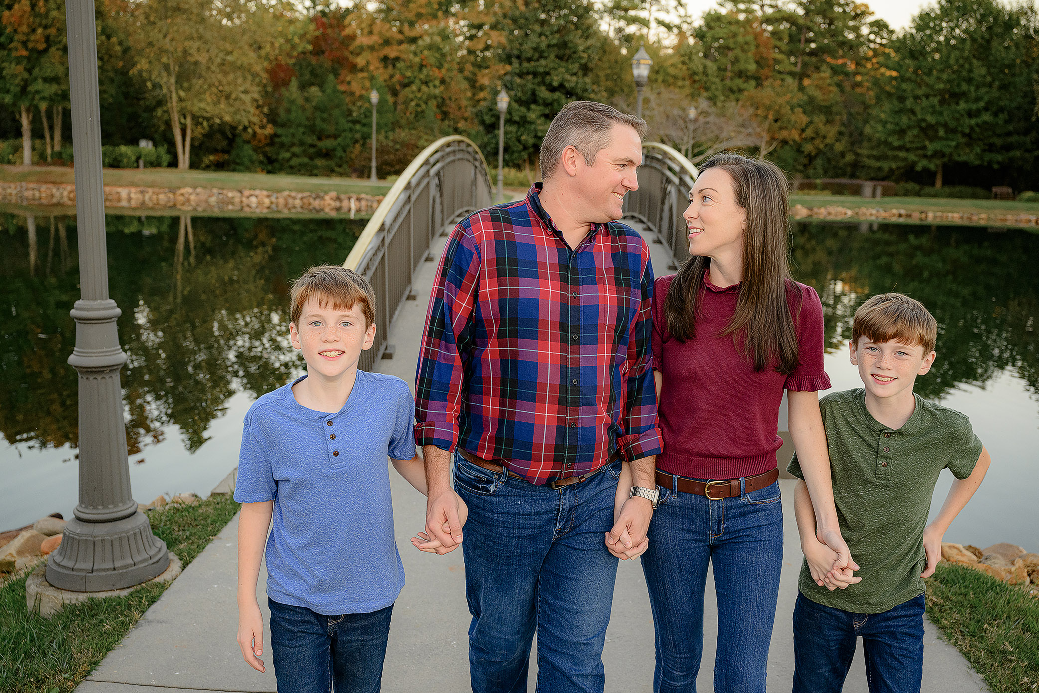 family of four walking hand in hand with mom and dad looking at each other and dressed in warm fall tones