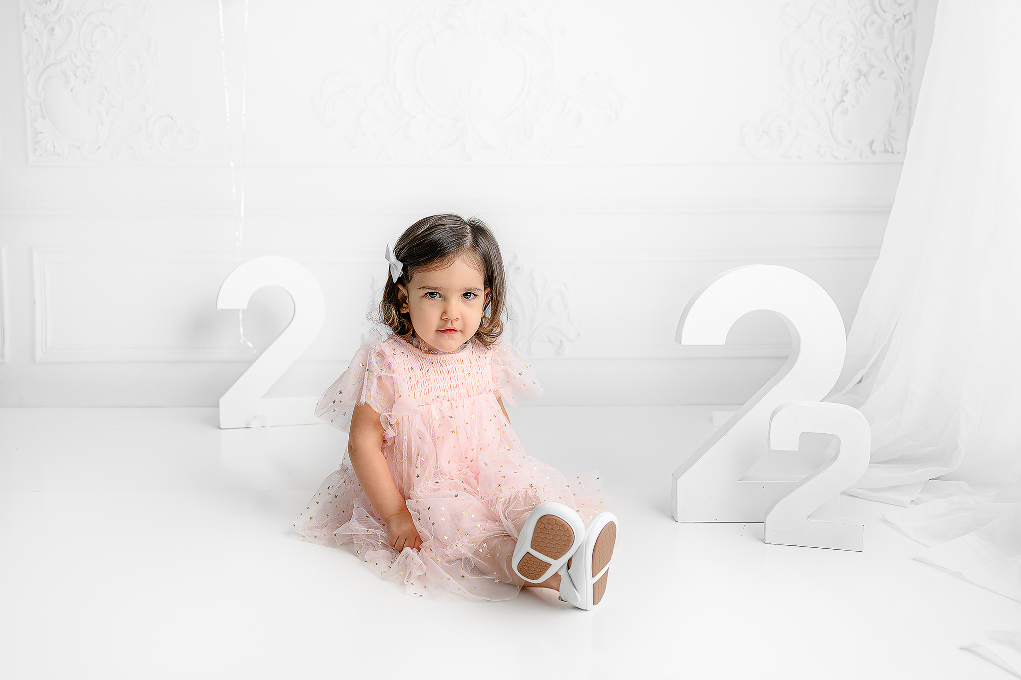Little girl sitting wearing white shoes and wearing a pink tulle dress with gold accents in the charlotte nc area studio