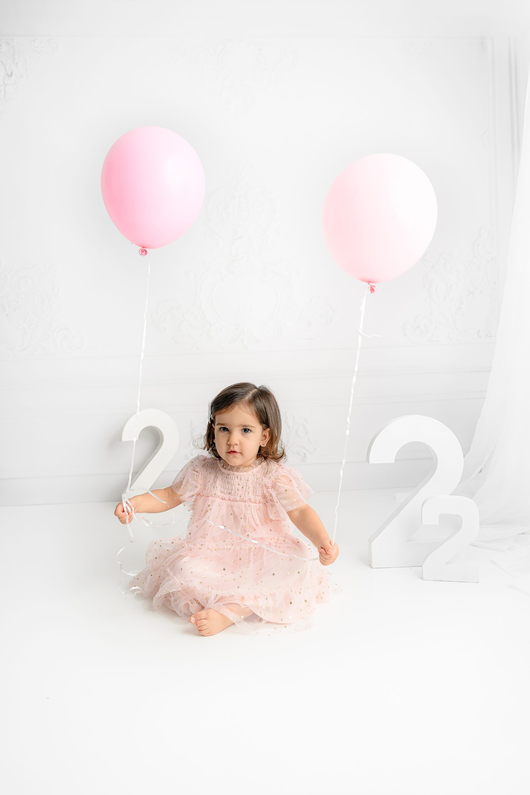 Little girl sitting holding balloons and giggling while wearing a pink tulle dress with gold accents in the charlotte nc area studio