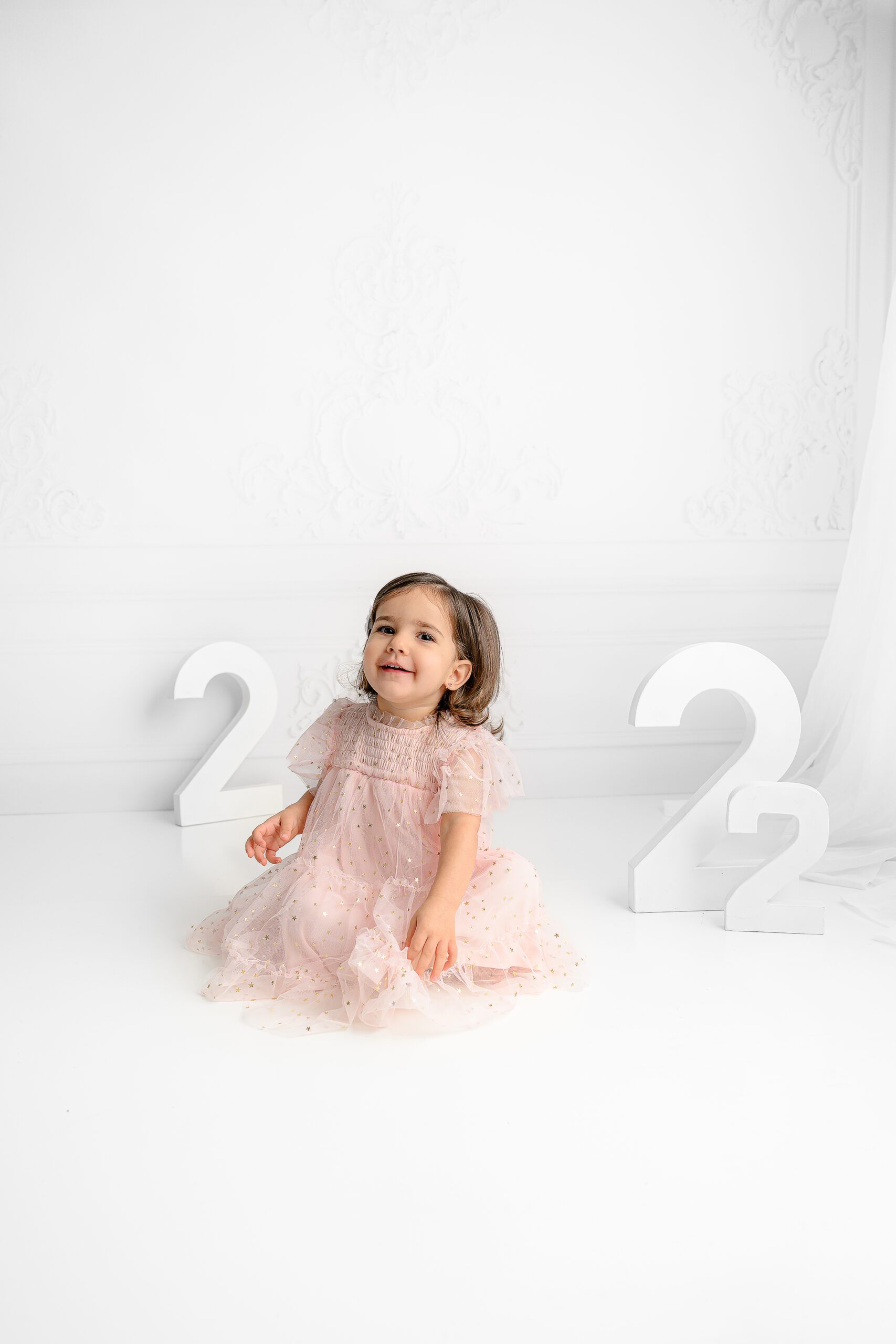 Little girl giggling while wearing a pink tulle dress with gold accents during her milestone session