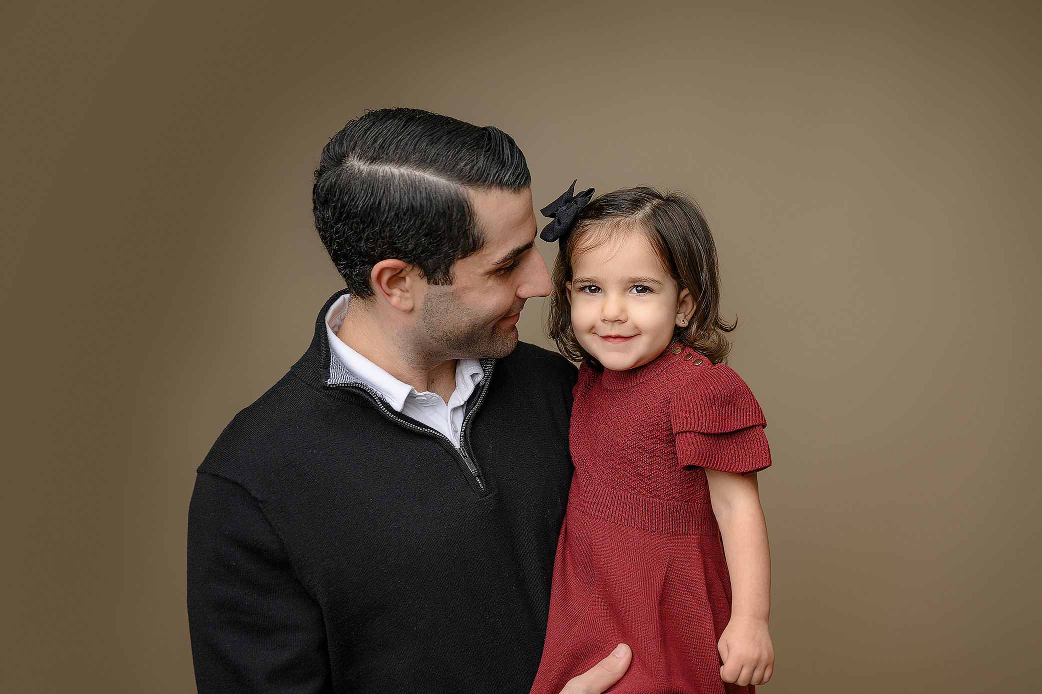 Dad dressed in black looking at his two year old daughter wearing a red dress and black hair bow