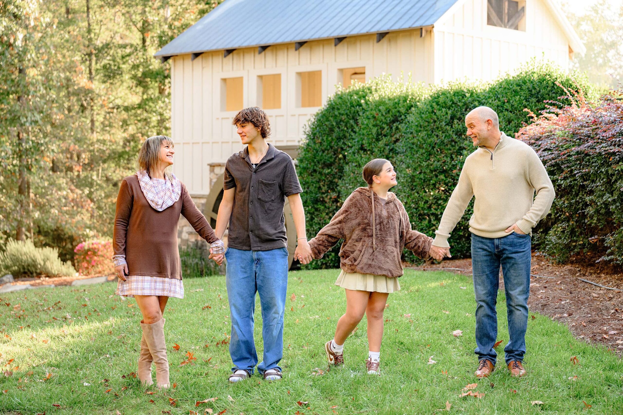 family of four dressed in brown tones standing together holding hands and looking at each other and laughing during their oldest sons grad session
