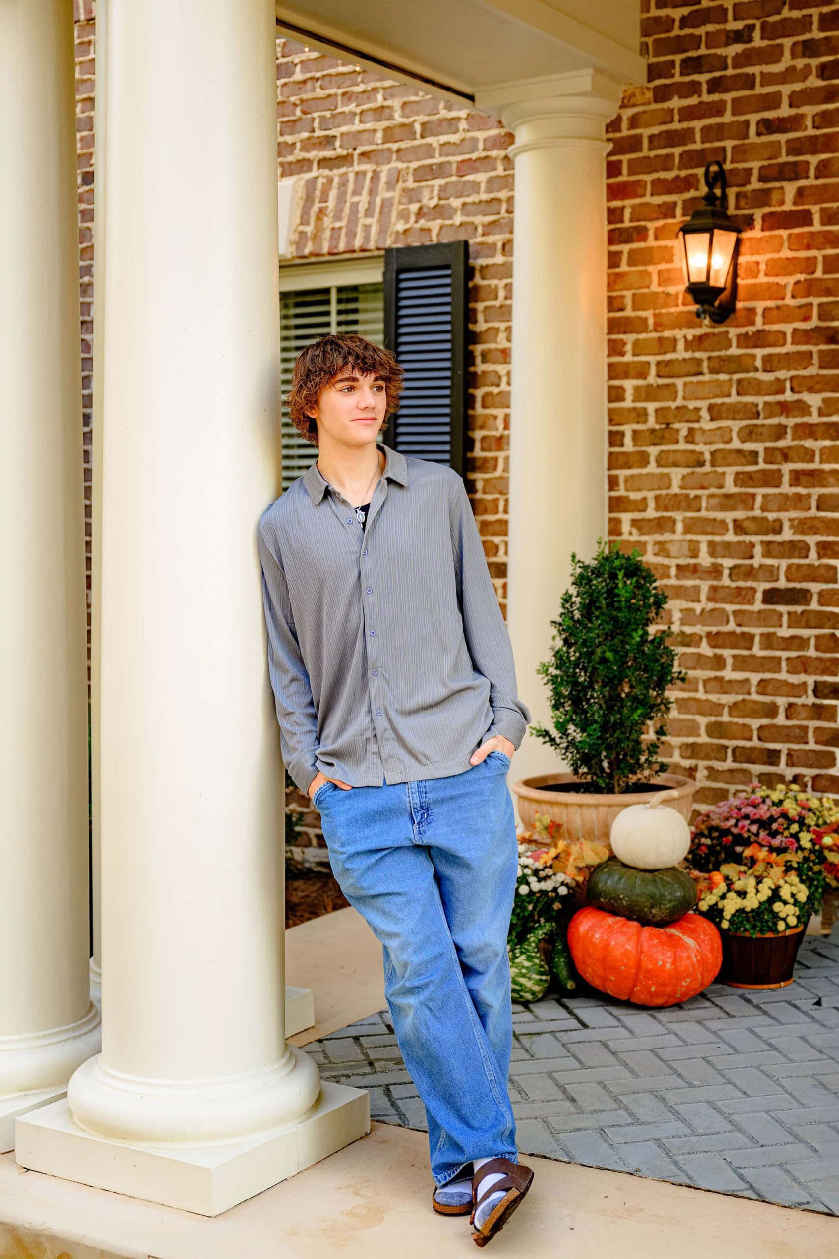 dark hair senior boy from cuthbertson high school in waxhaw, nc standing leaning against a building column wearing jeans and a grey shirt with his hands in his pockets